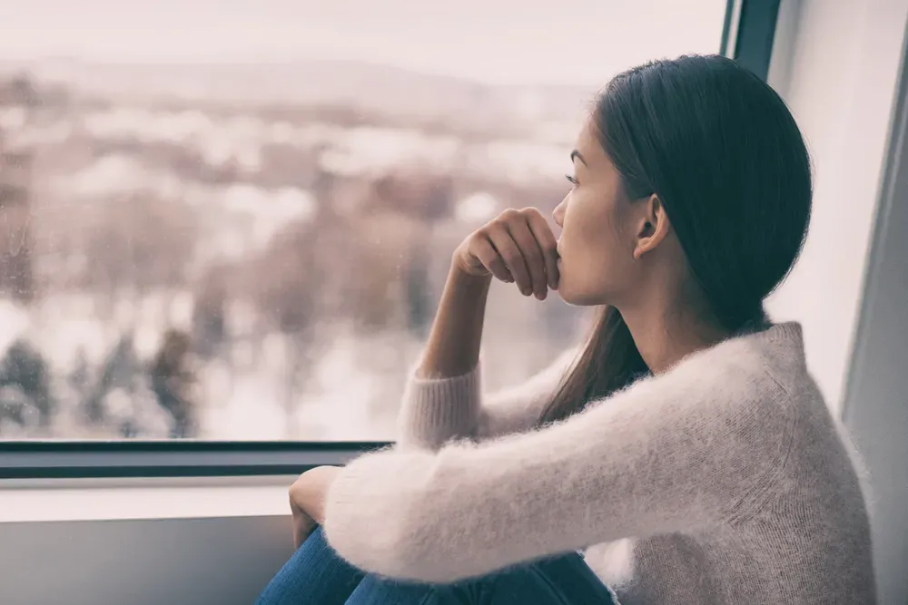 A woman is sitting on a window sill looking out the window.