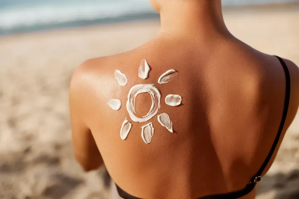 A woman is applying sunscreen to her back on the beach.