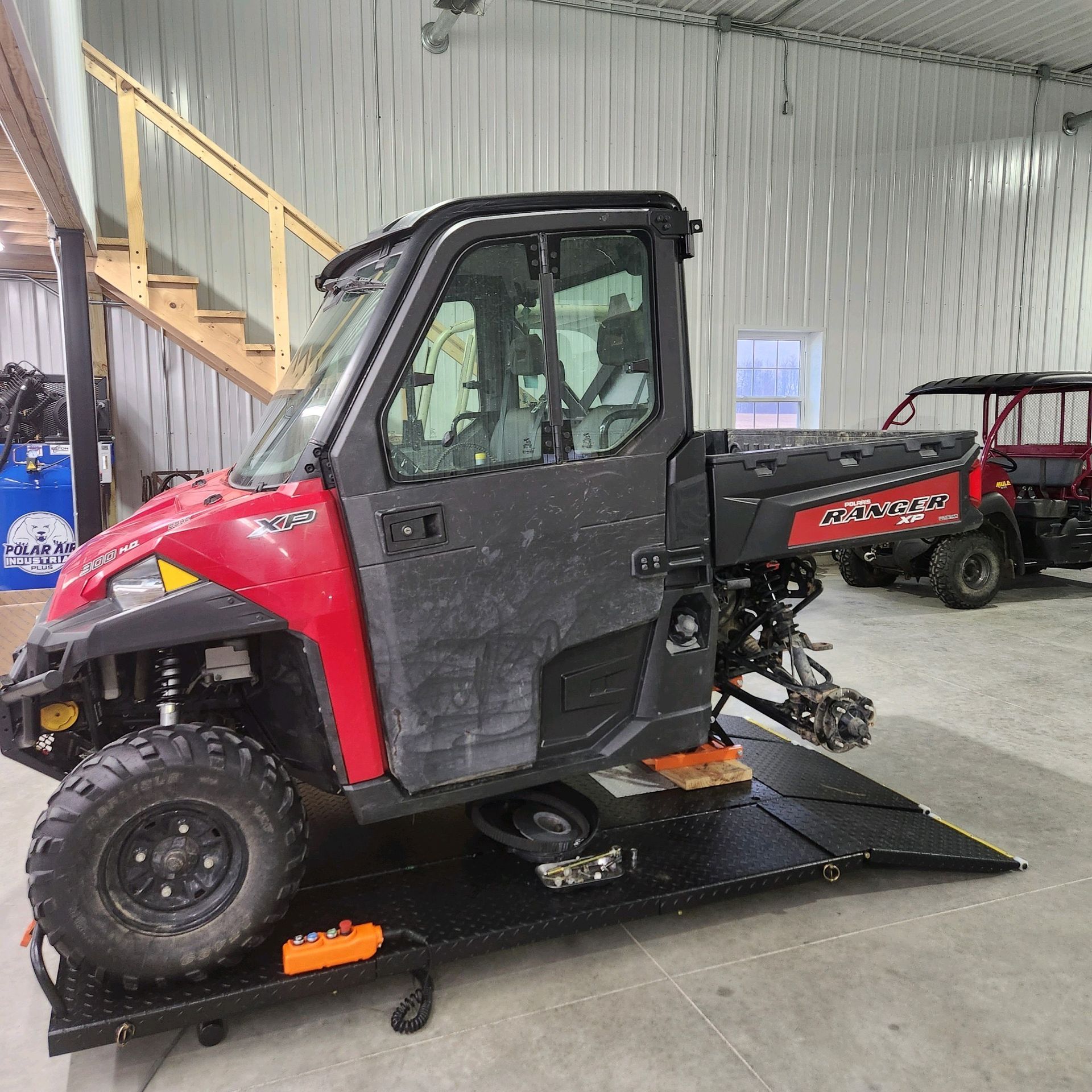 Red and black Polaris Ranger UTV on a black platform lift inside a shop.