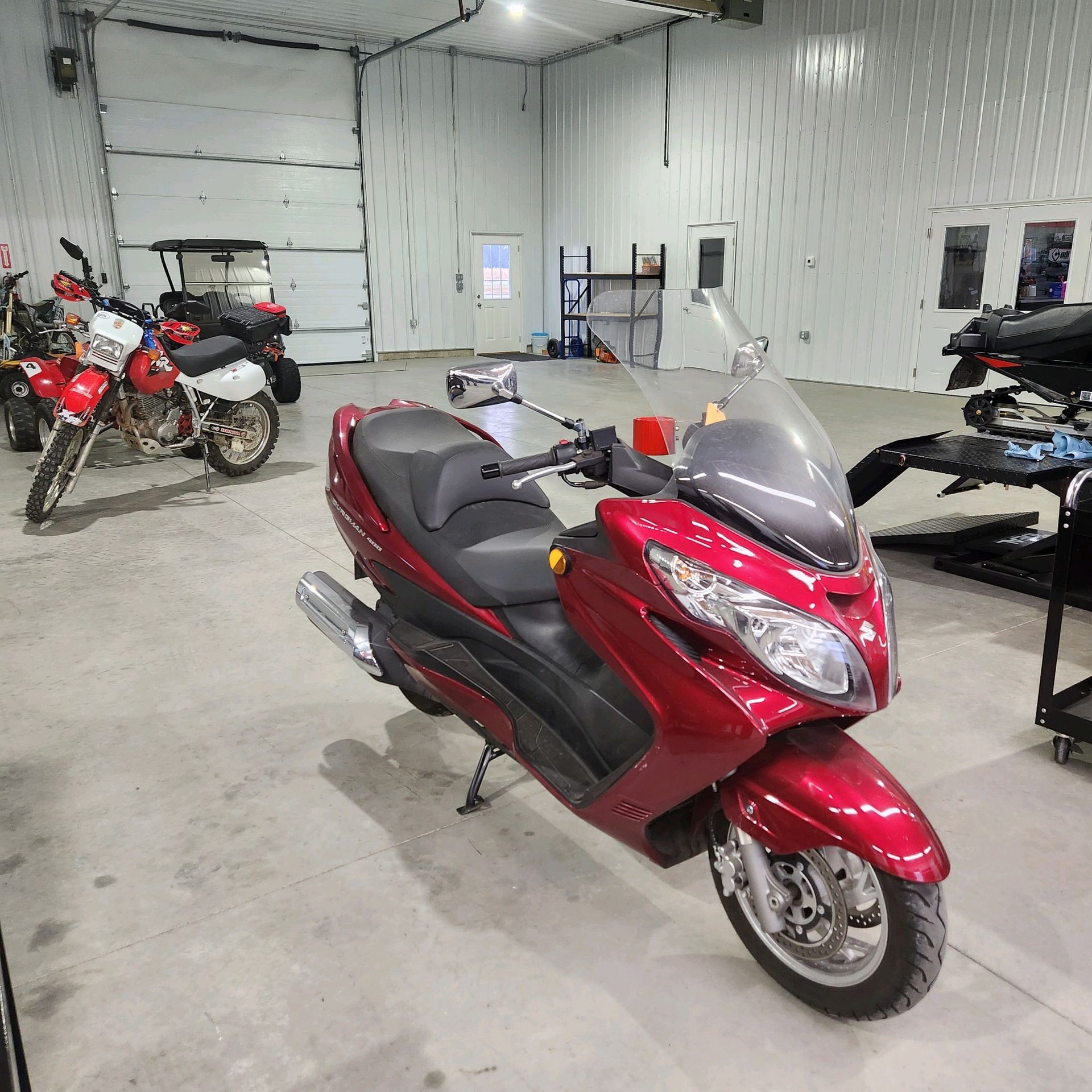 Red scooter in a garage with a motorcycle and workspace.