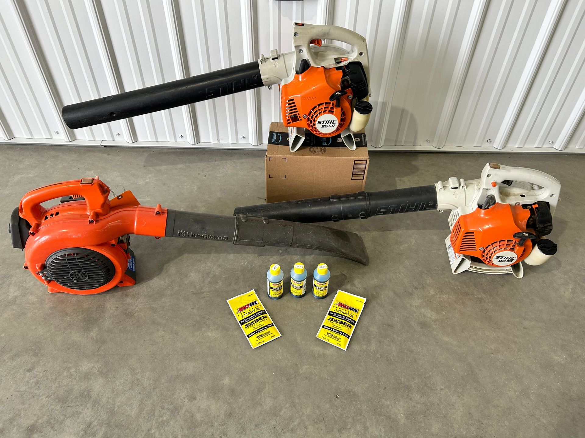 Two orange and white leaf blowers with accessories on a gray surface.
