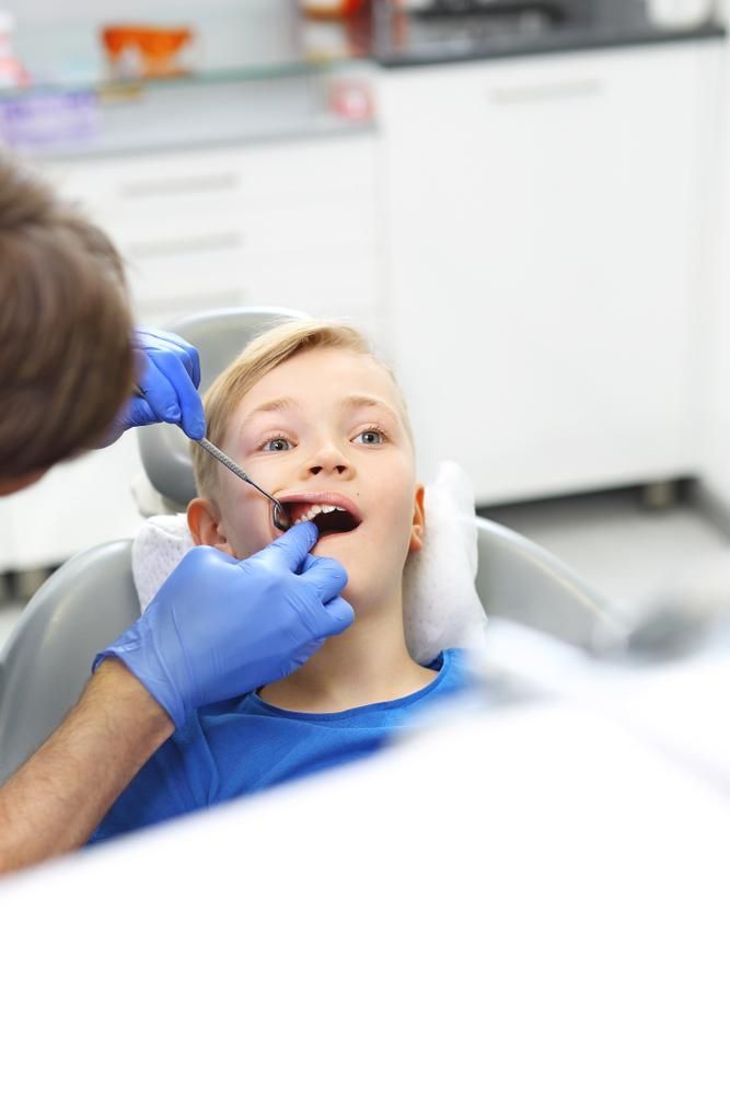 A Boy Is Sitting in A Dental Chair Getting His Teeth Examined by A Dentist — Peter McLennan Denture Clinic in Grafton, NSW