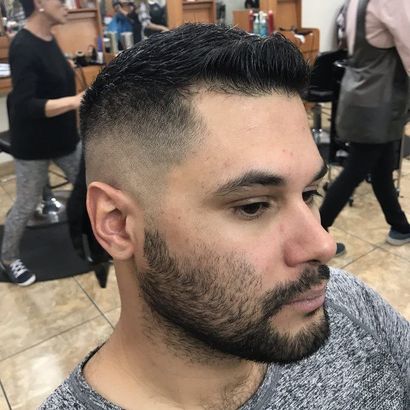 a man with a beard is getting his hair cut in a salon