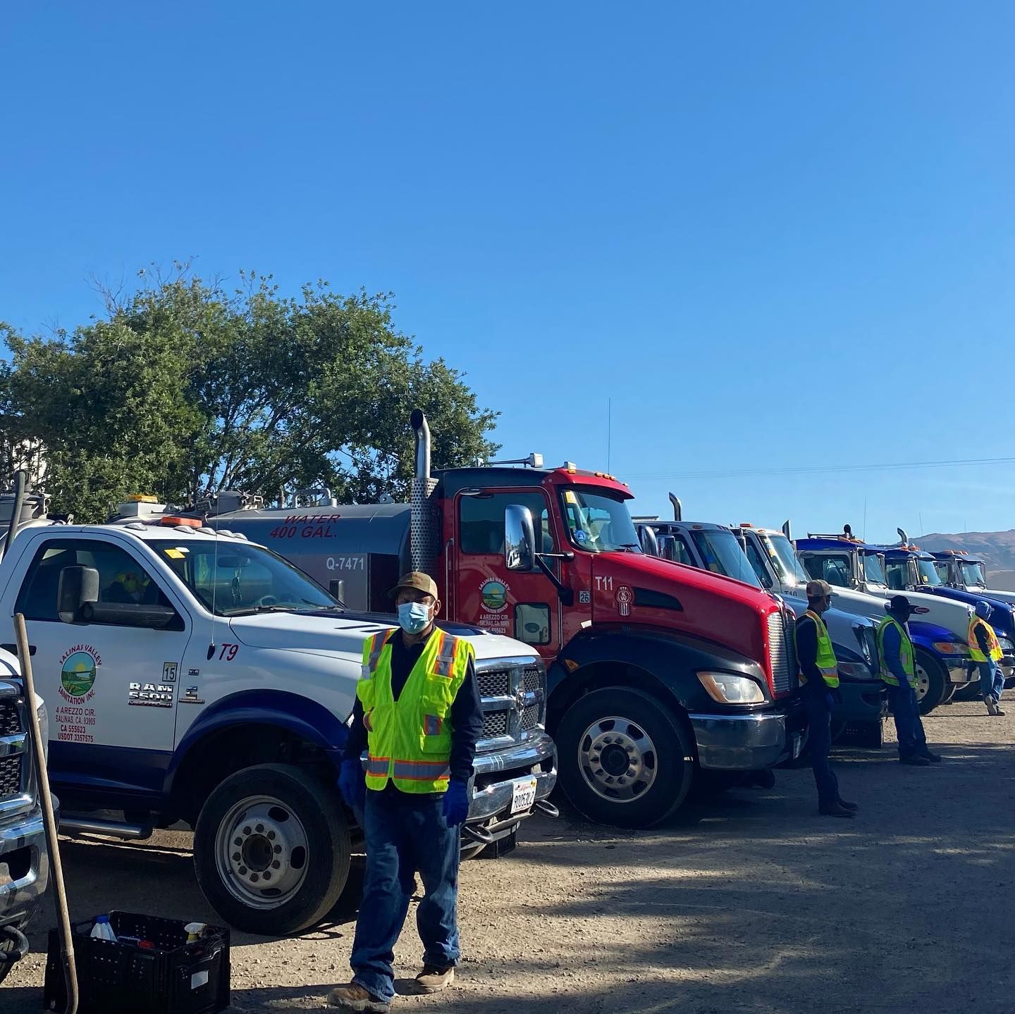 A man wearing a mask stands in front of a row of trucks