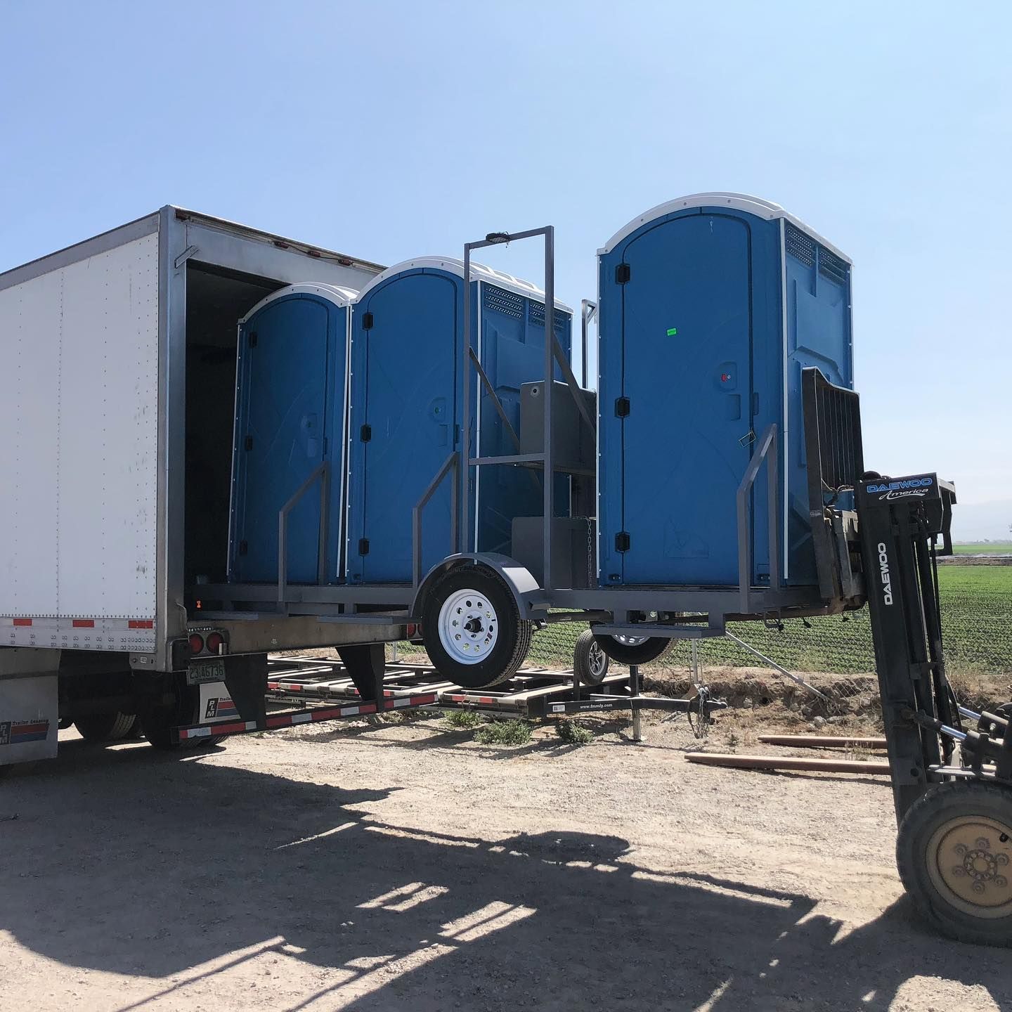 A forklift is lifting a trailer full of blue portable toilets