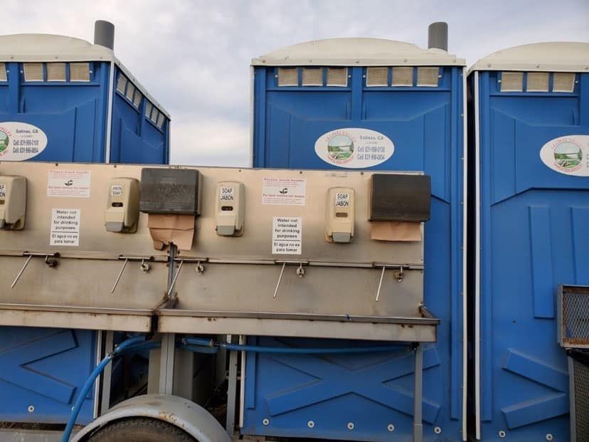 Three blue portable toilets with sinks and soap dispensers