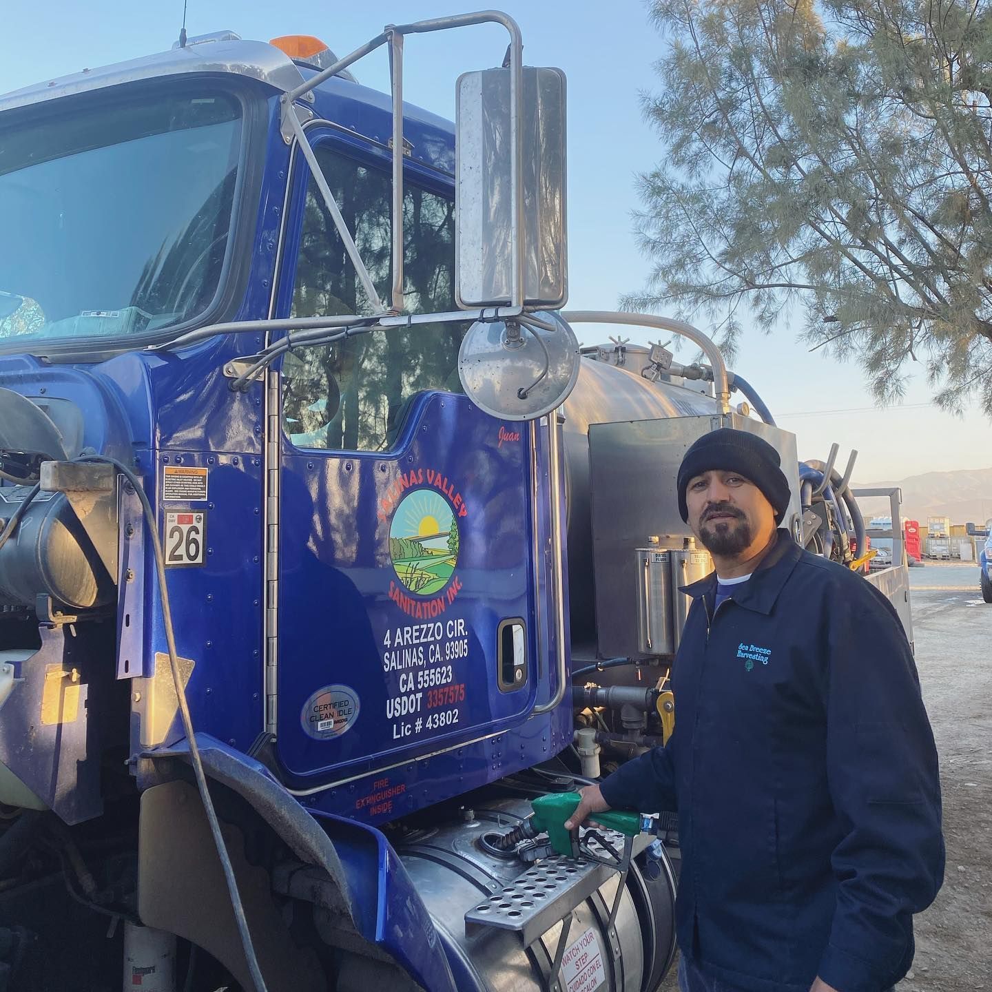 A man is standing in front of a blue truck with the number 26 on it