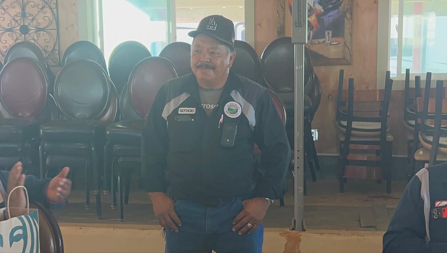 A man with a mustache is standing in a room with chairs.