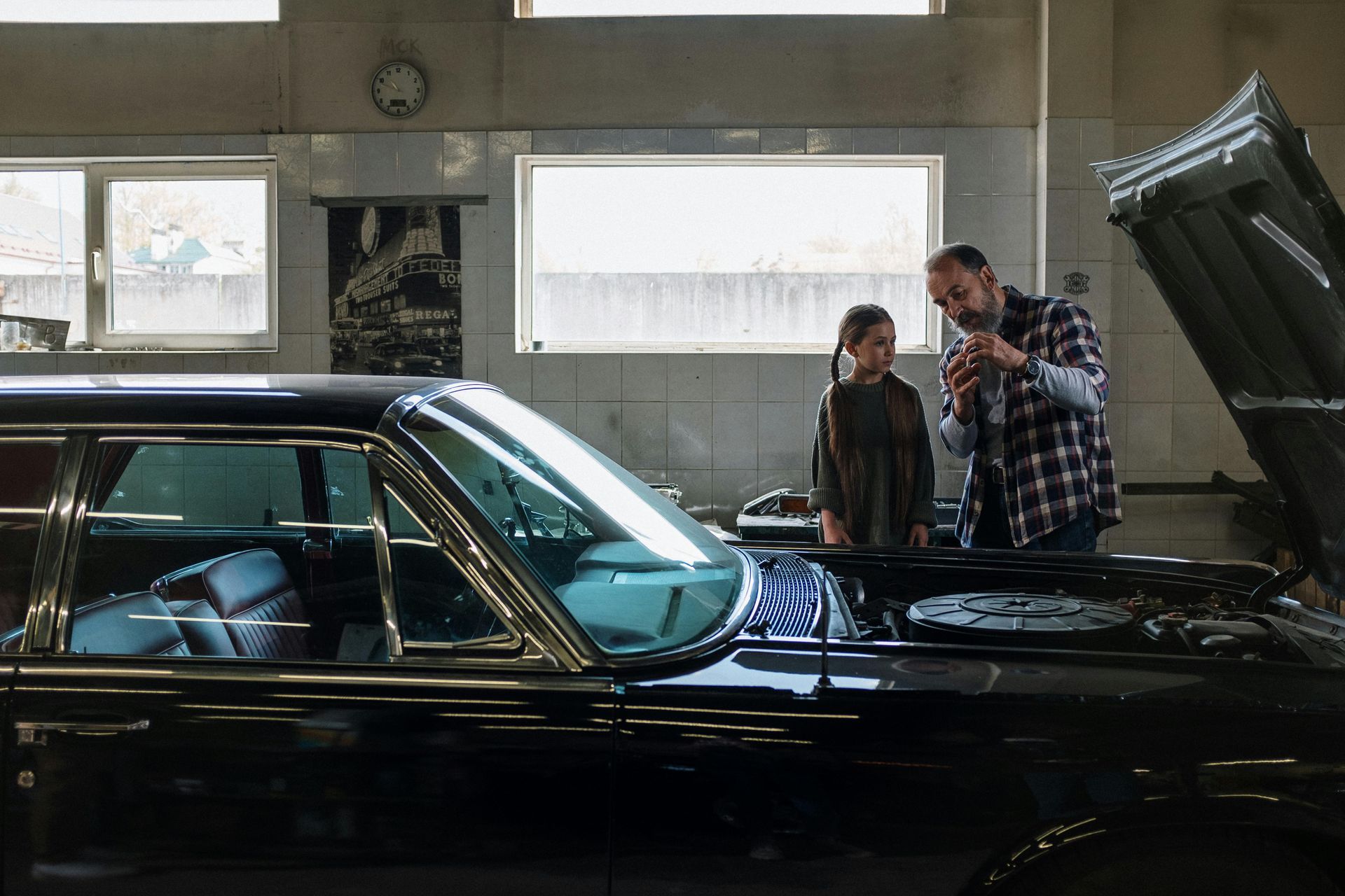 A man and a boy are looking at a car in a garage.