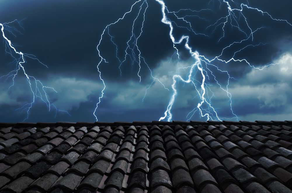 Lightning strikes over a tiled roof at night