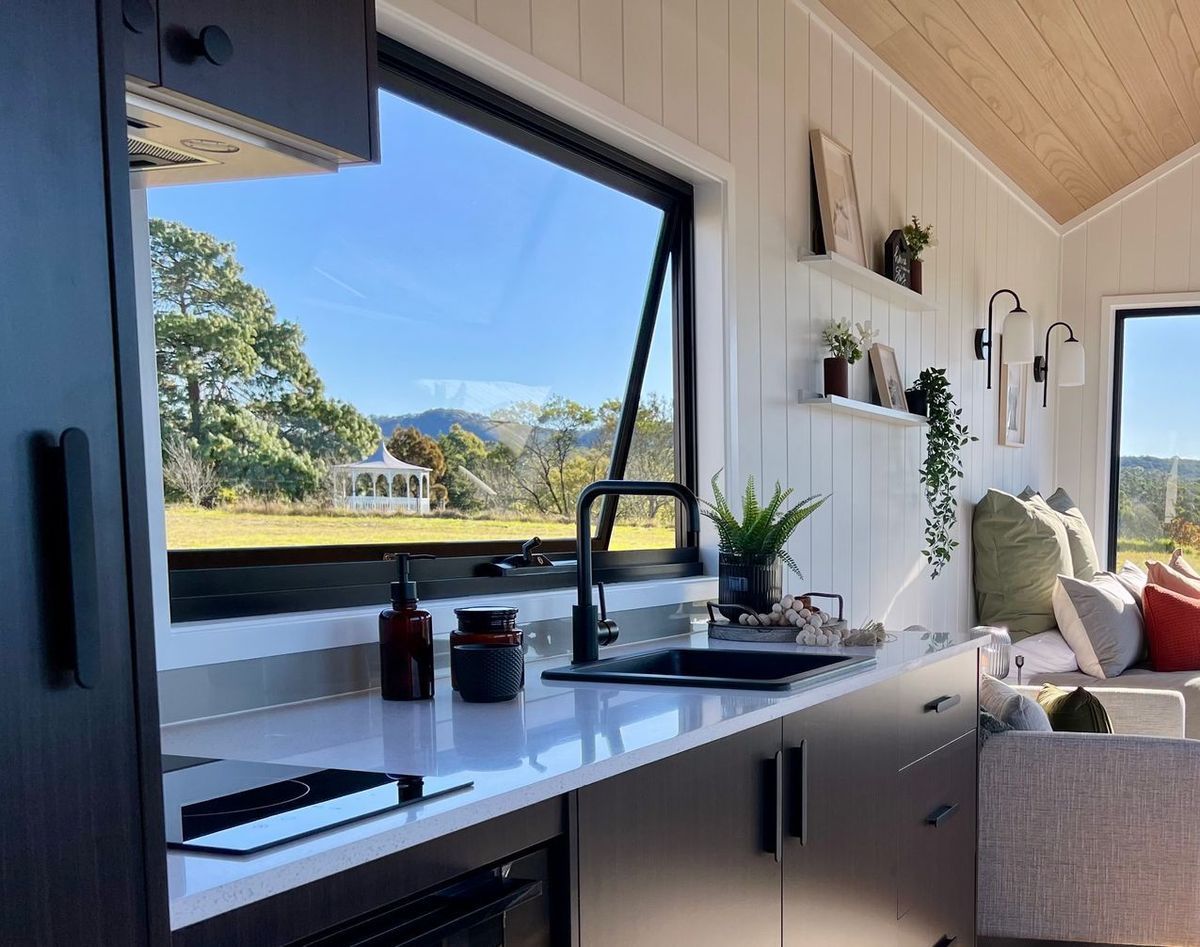 Modern tiny home kitchen with a large window framing a scenic outdoor view.