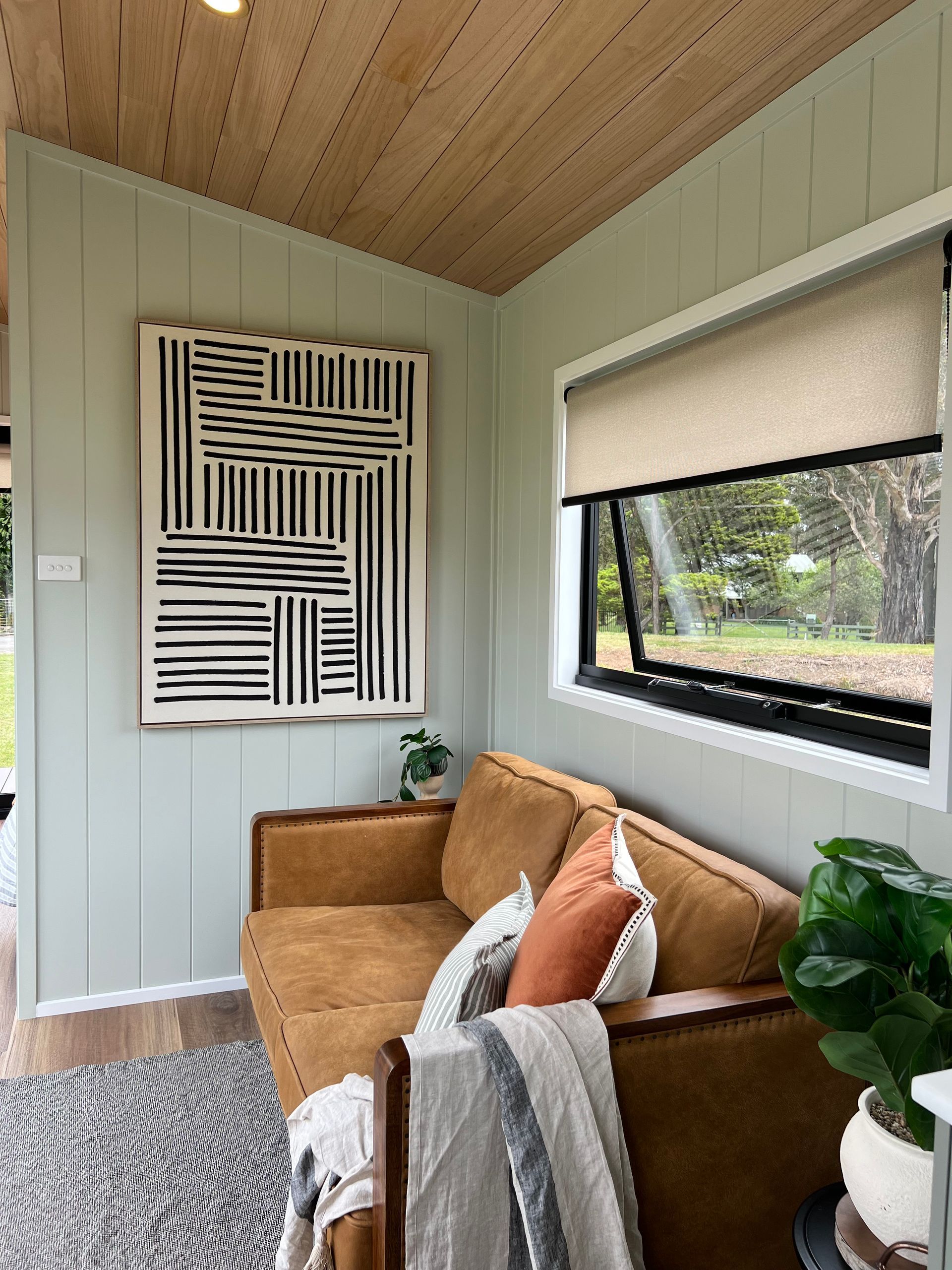 Cozy interior with a brown leather couch, abstract art, and a window. Light green walls and a wood ceiling.