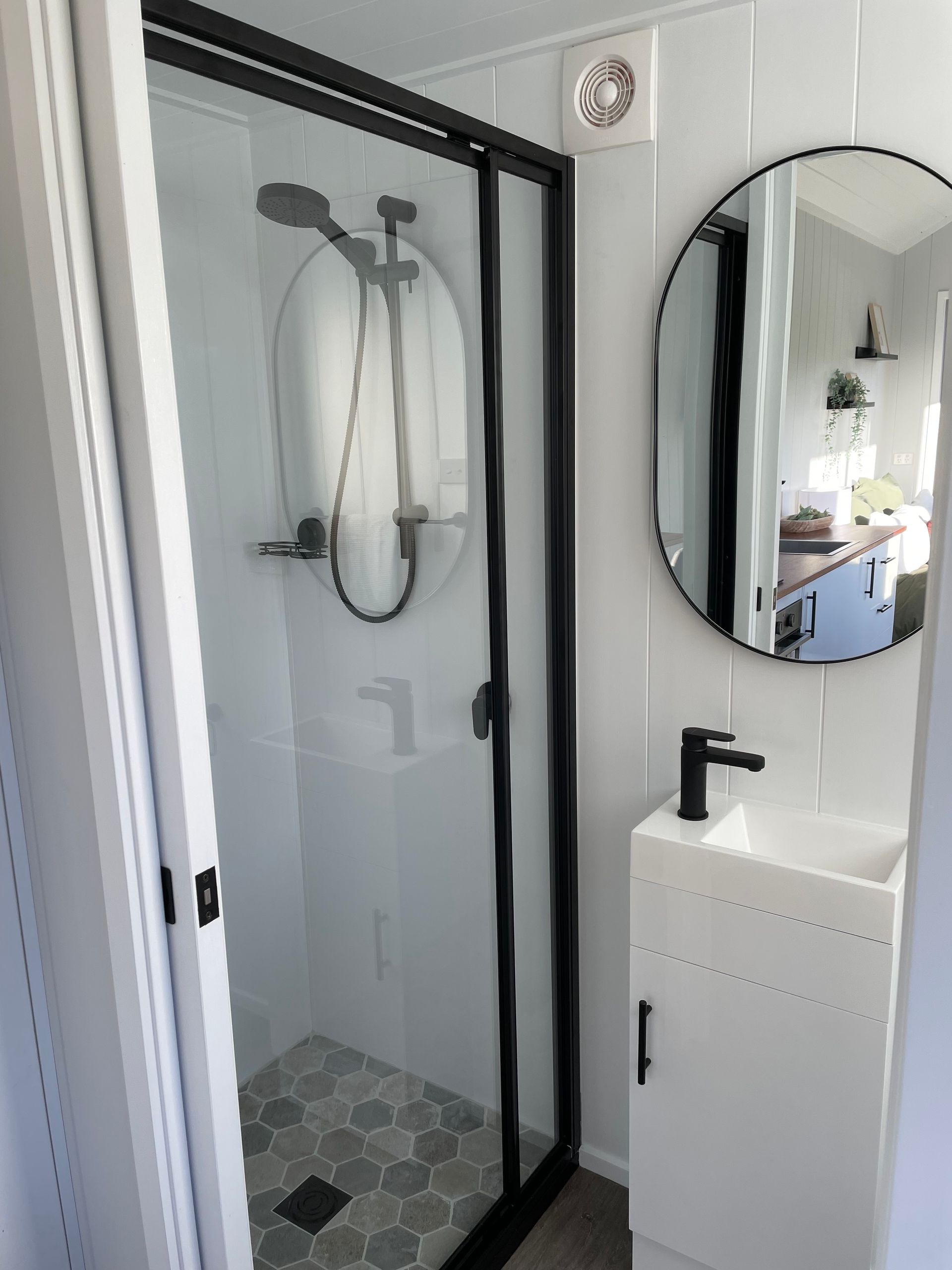 Small modern bathroom with a shower, sink, and round mirror.