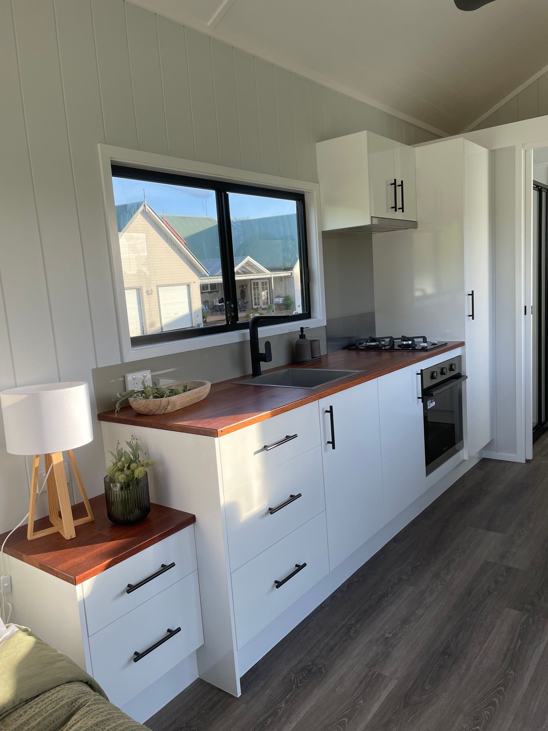 Small white kitchen with wood countertop, black accents, and a window overlooking a building.
