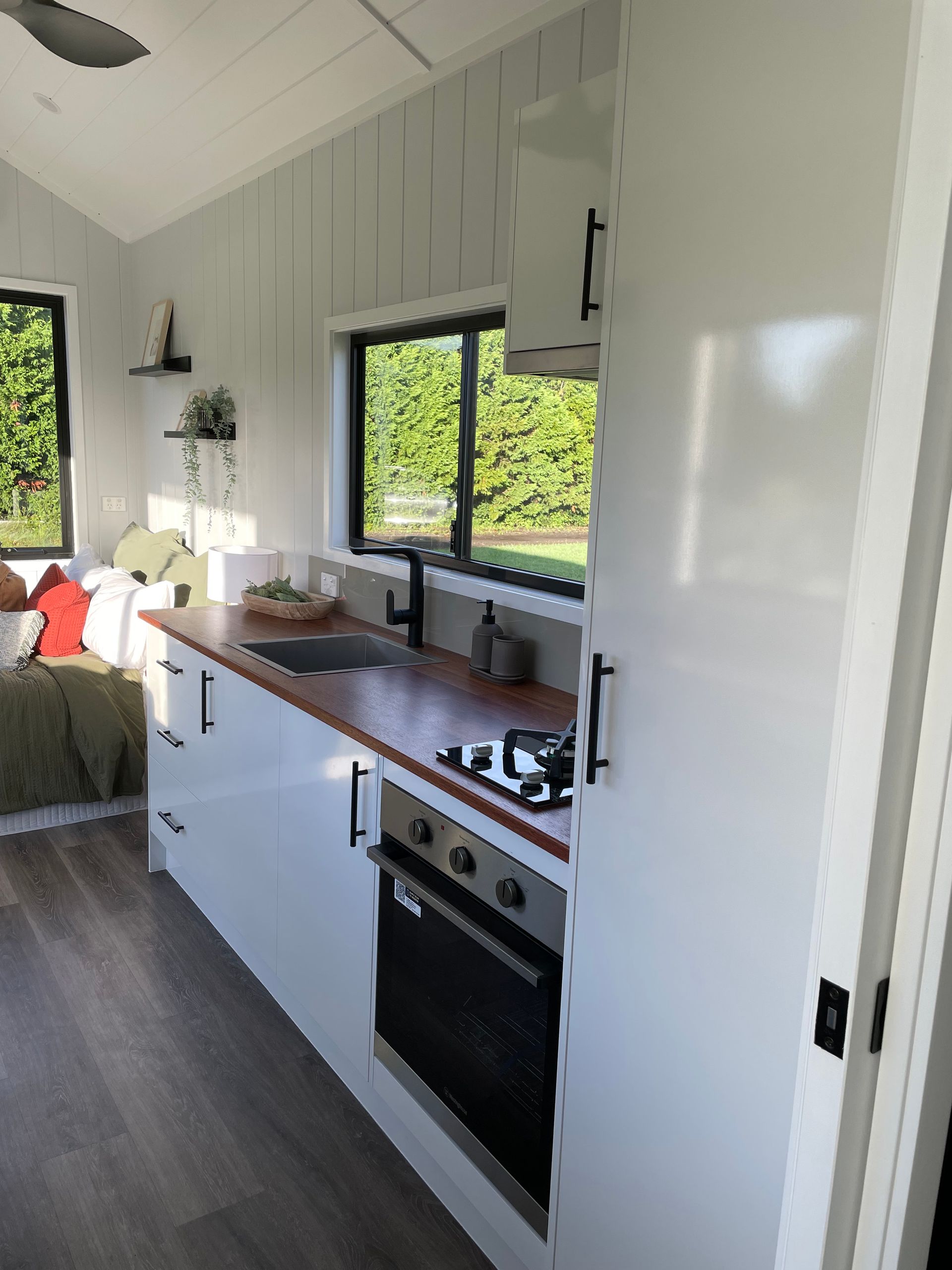 Modern kitchen with white cabinets, wooden countertop, black appliances, and window with outside view.
