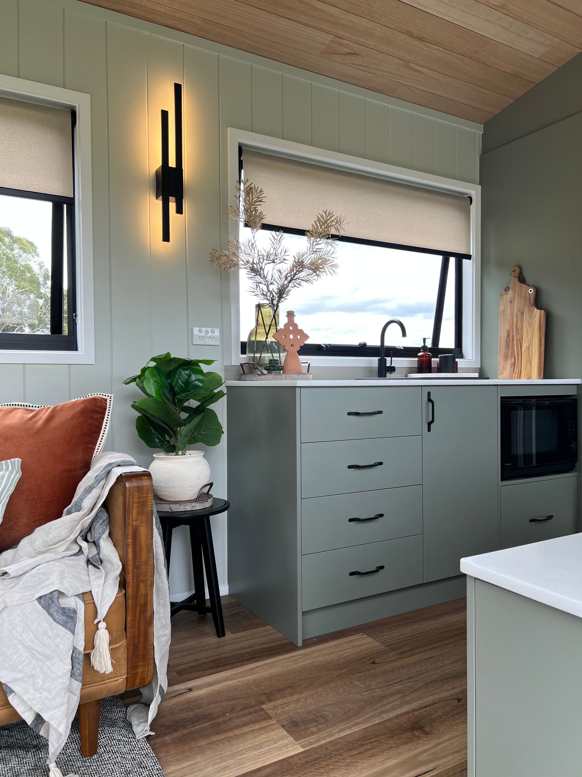 Small kitchen with sage green cabinets, black hardware, and wood accents.
