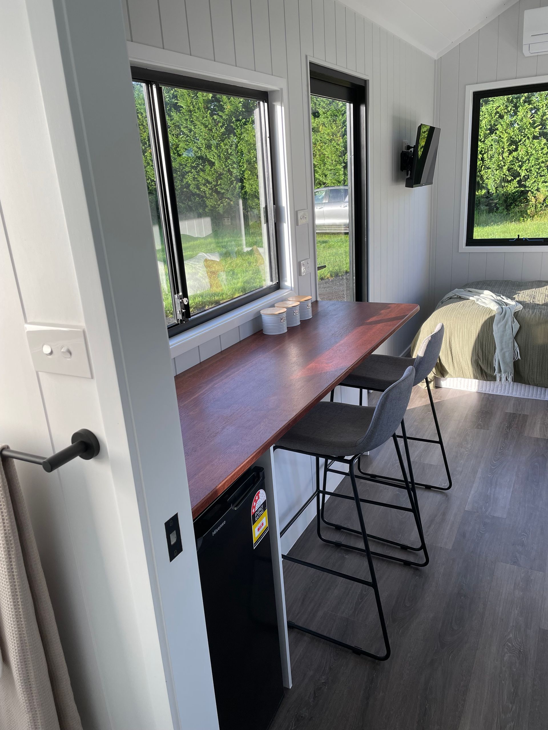 Interior shot: Tiny home with a bar table, two stools, and a bed near a window.