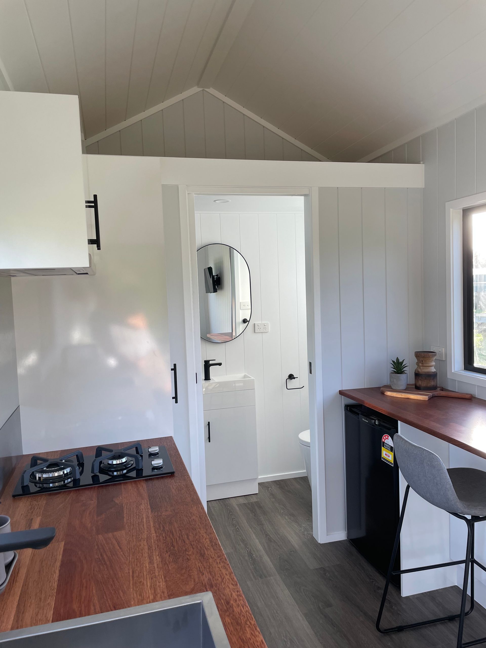Small cabin interior with kitchen and bathroom visible; white walls, dark wood counters, bar, and small fridge.
