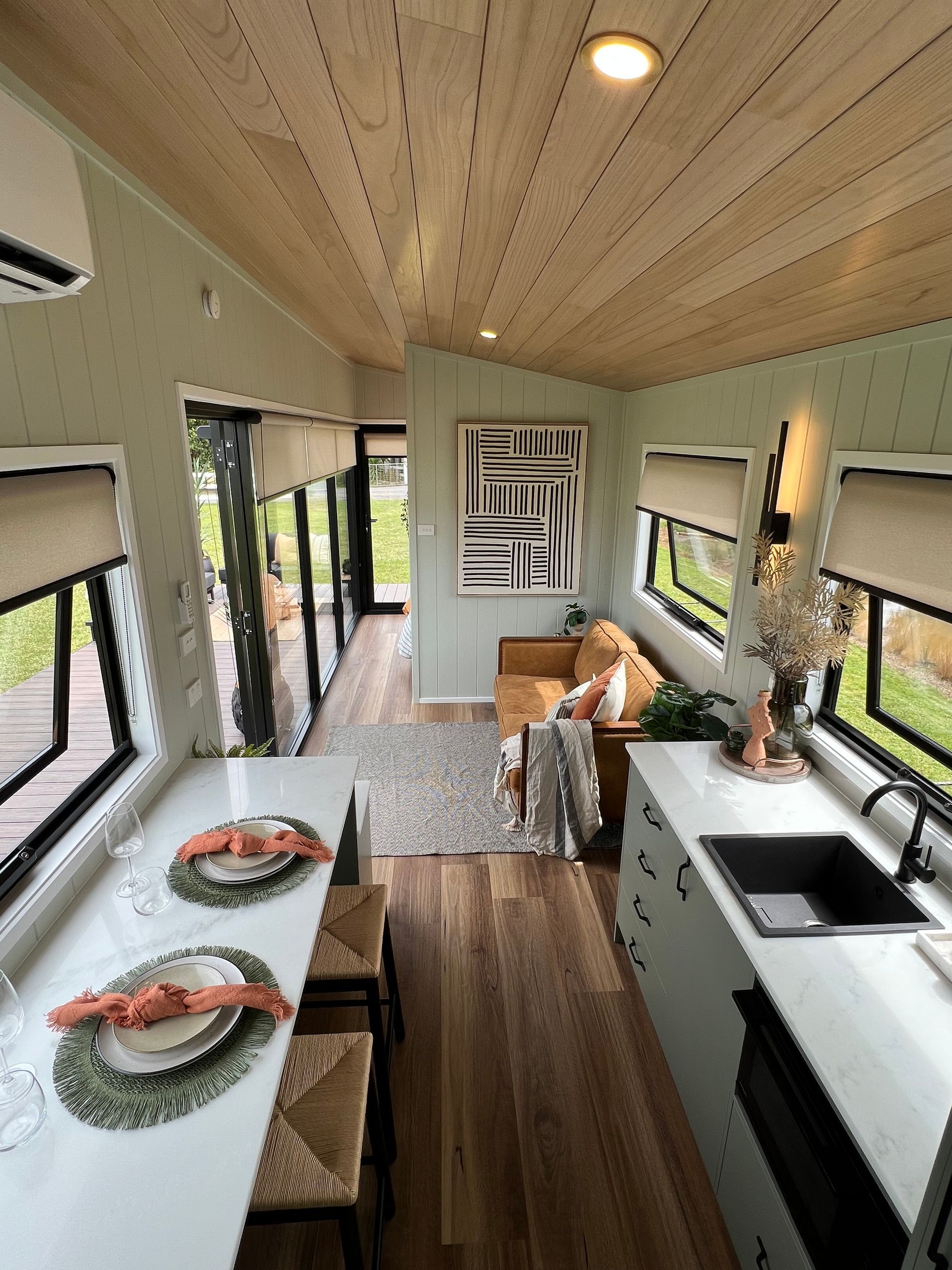 Interior of a tiny home with pale green walls, wooden floors, and a light wood ceiling.