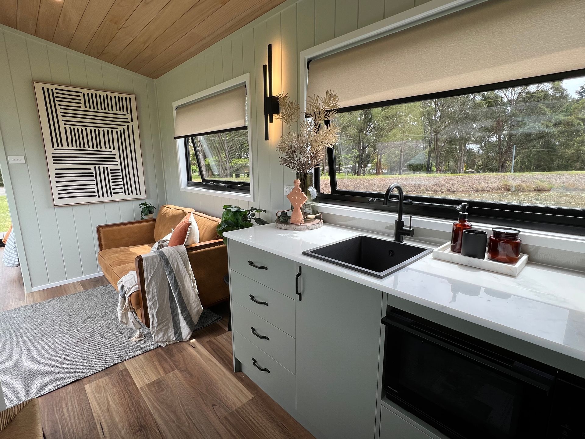 Cozy interior with a small kitchen and a seating area. Light green walls, brown sofa, and a large window overlooking a view.