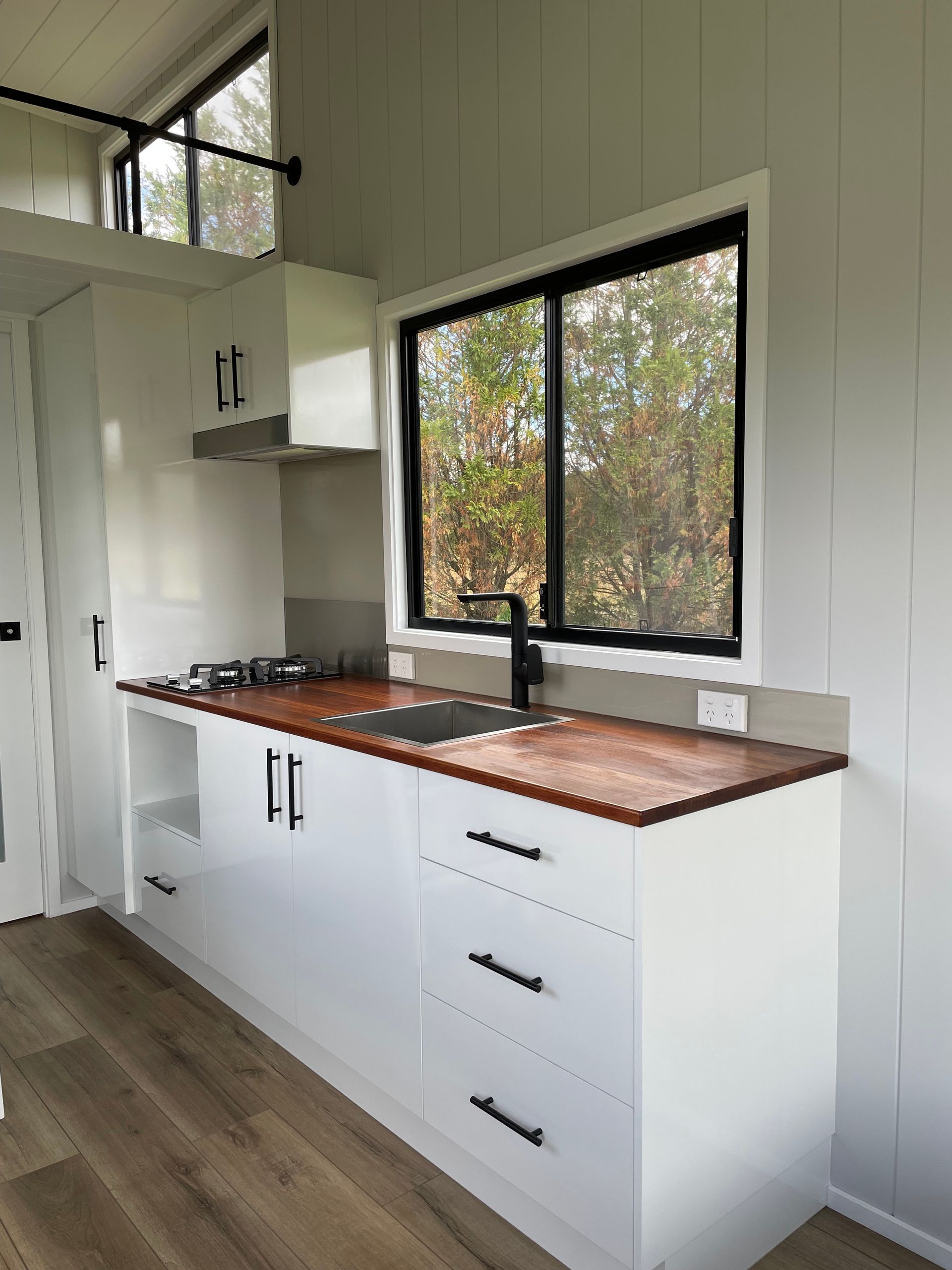 White kitchen with wood countertop, black faucet and cabinets, and a large window.