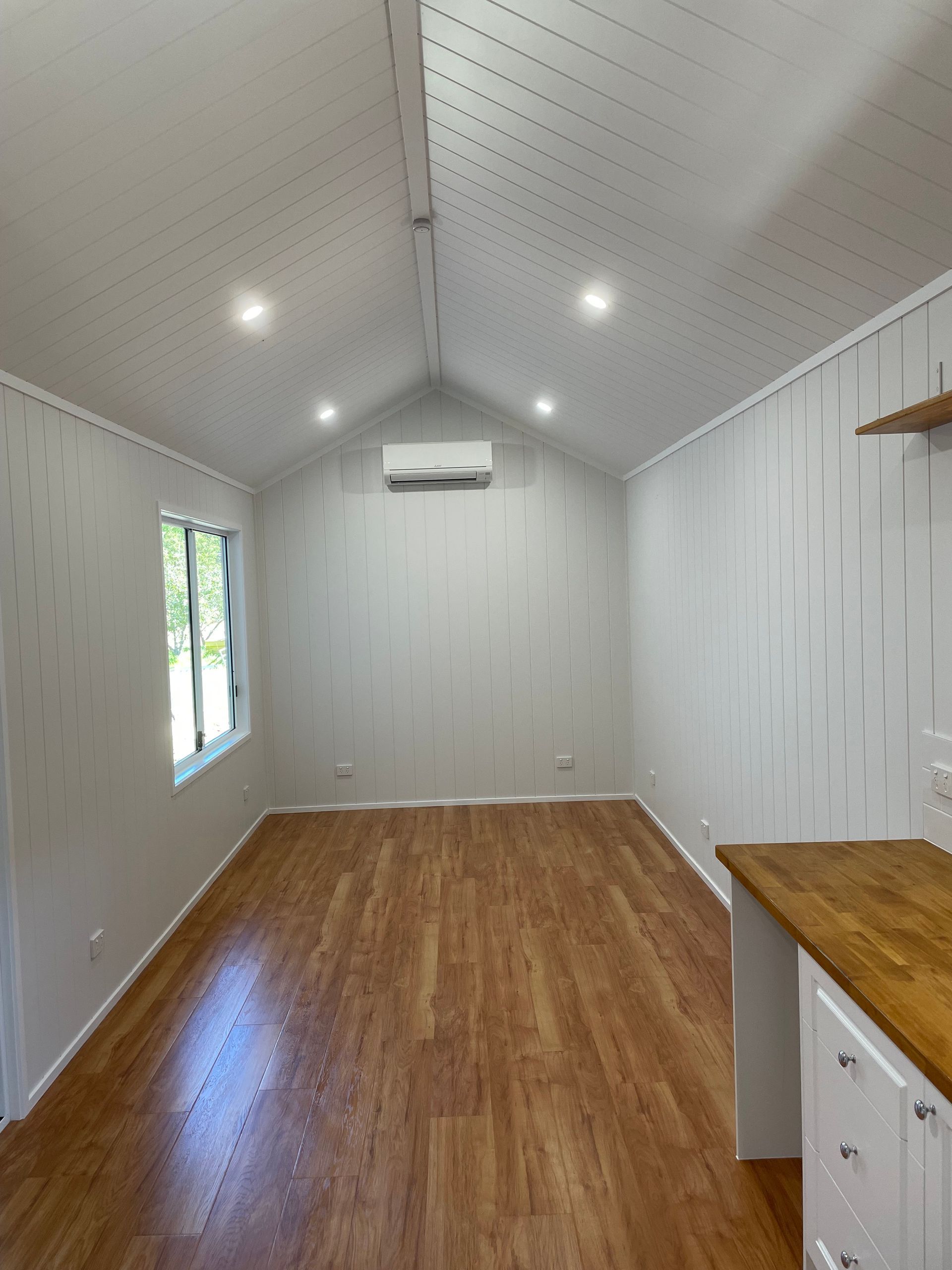 Interior view of a small room with white walls, wood floor, and an air conditioner.