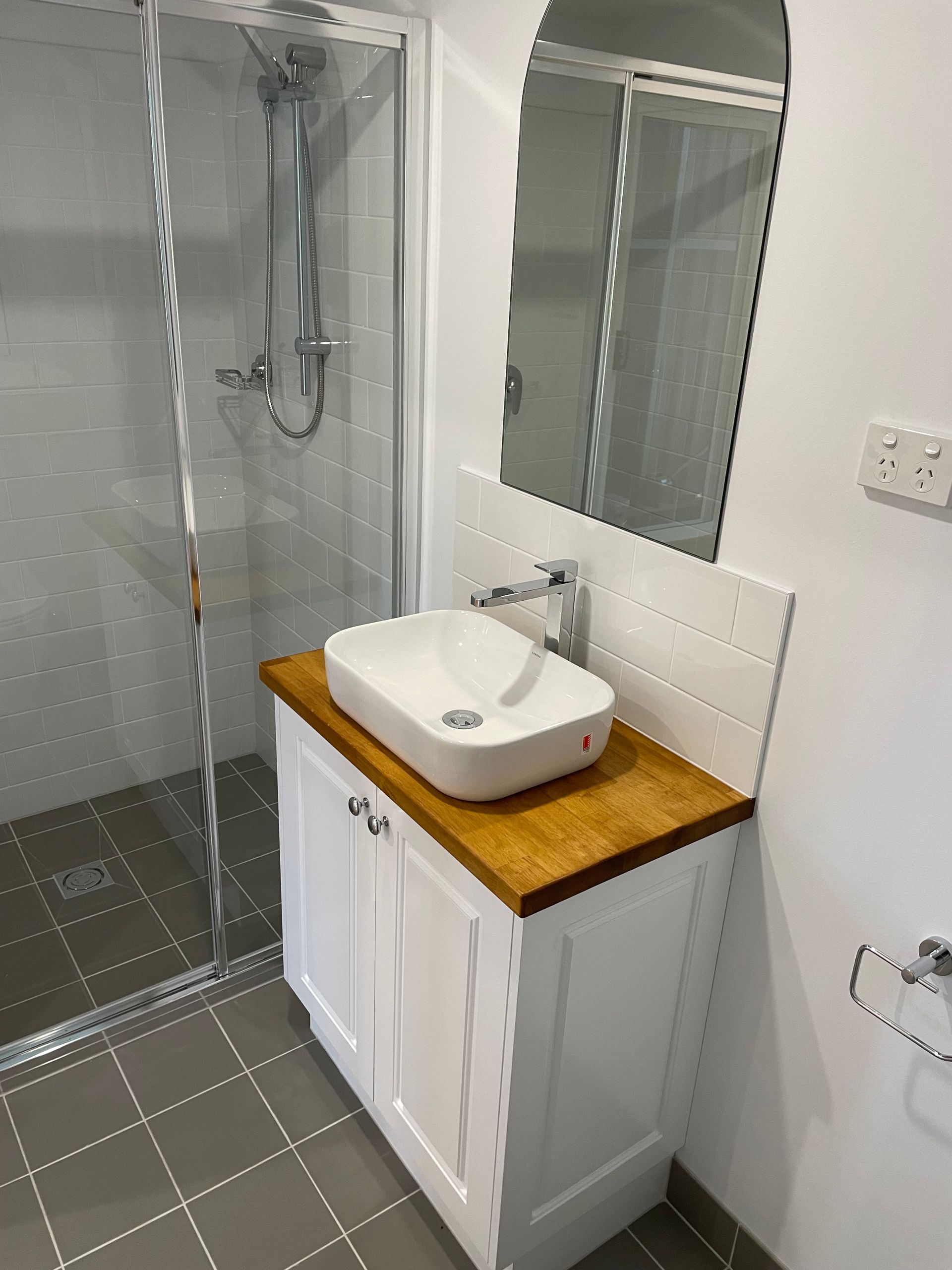Bathroom with white cabinet, wooden countertop, vessel sink, and shower. Gray tiled floor and wall.