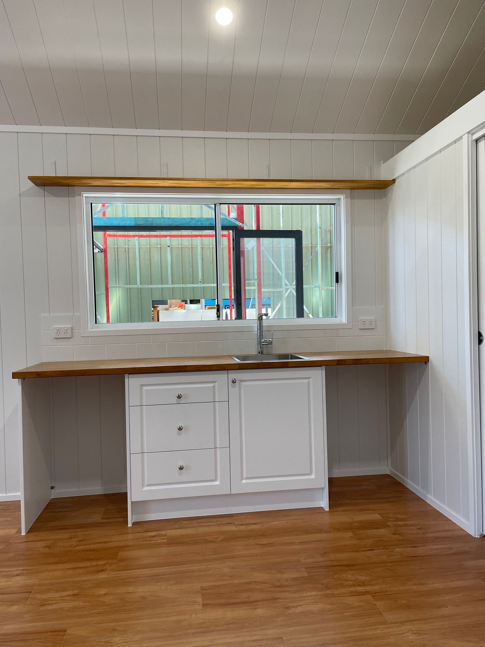 White kitchen with wood countertops, sink, cabinets, window, and a shelf.