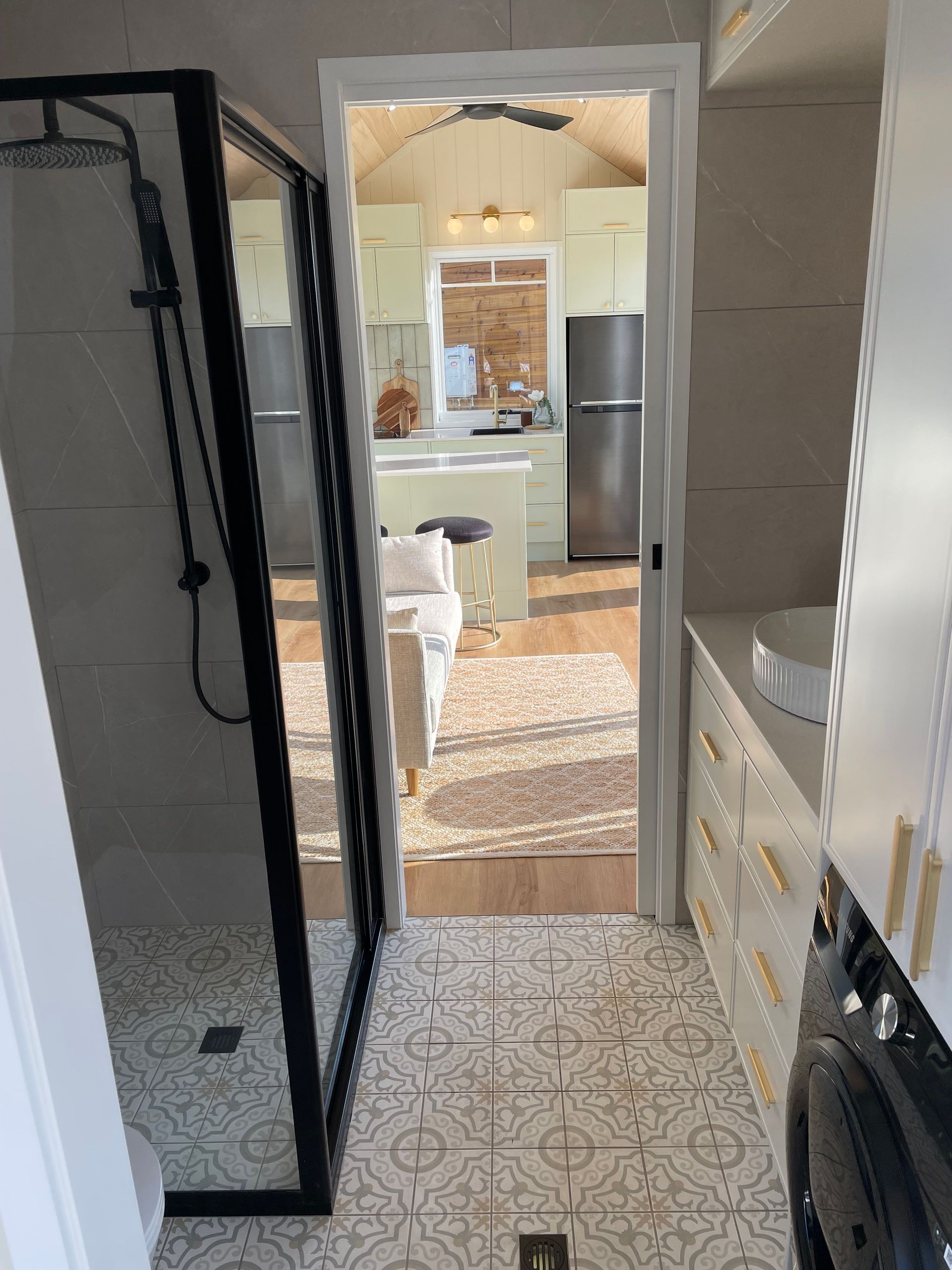 Bathroom with shower and door leading to kitchen; light color scheme, black accents.