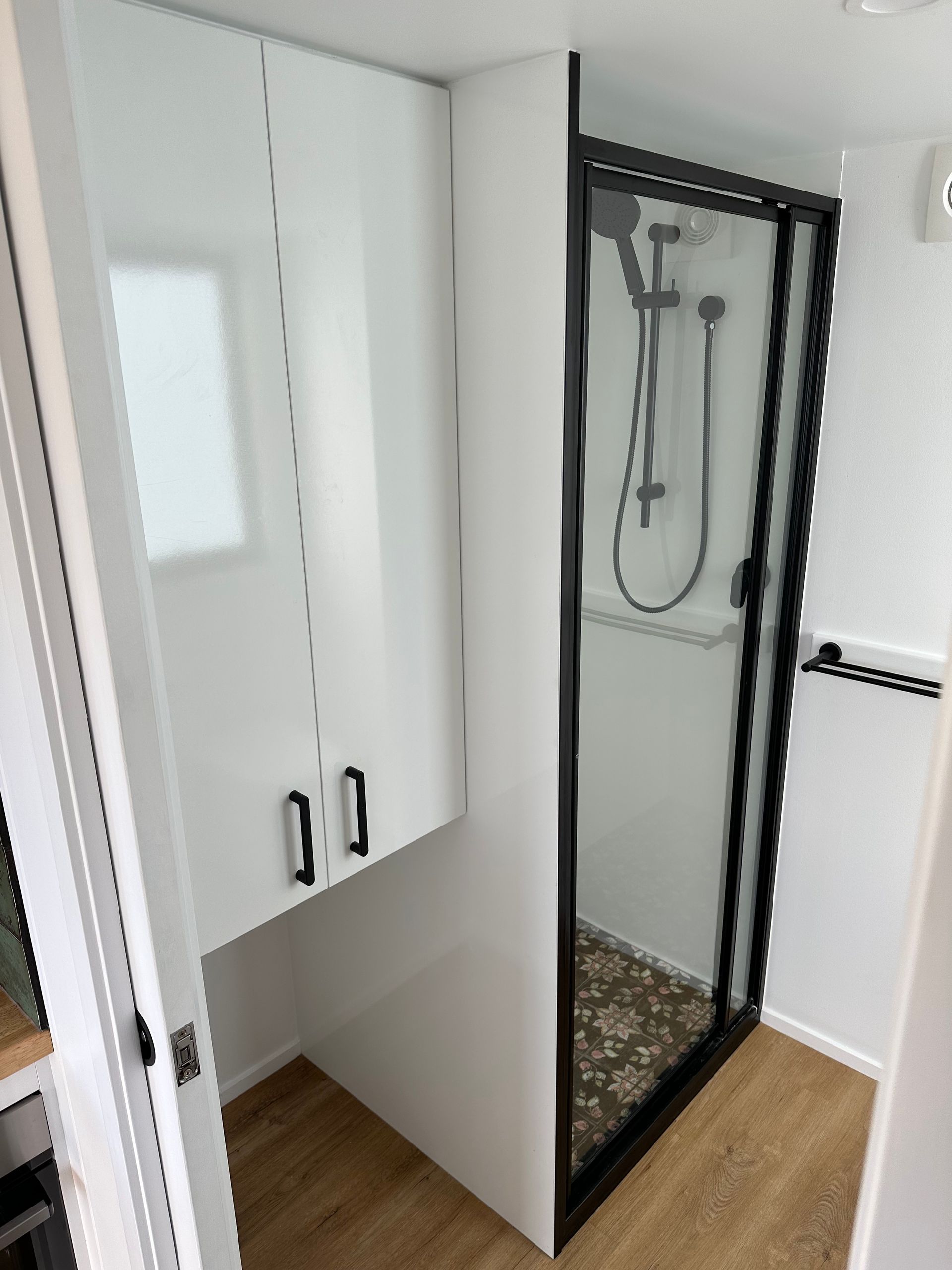 White bathroom with a shower, cabinetry, and a frosted window. Black framed shower with pebble floor.