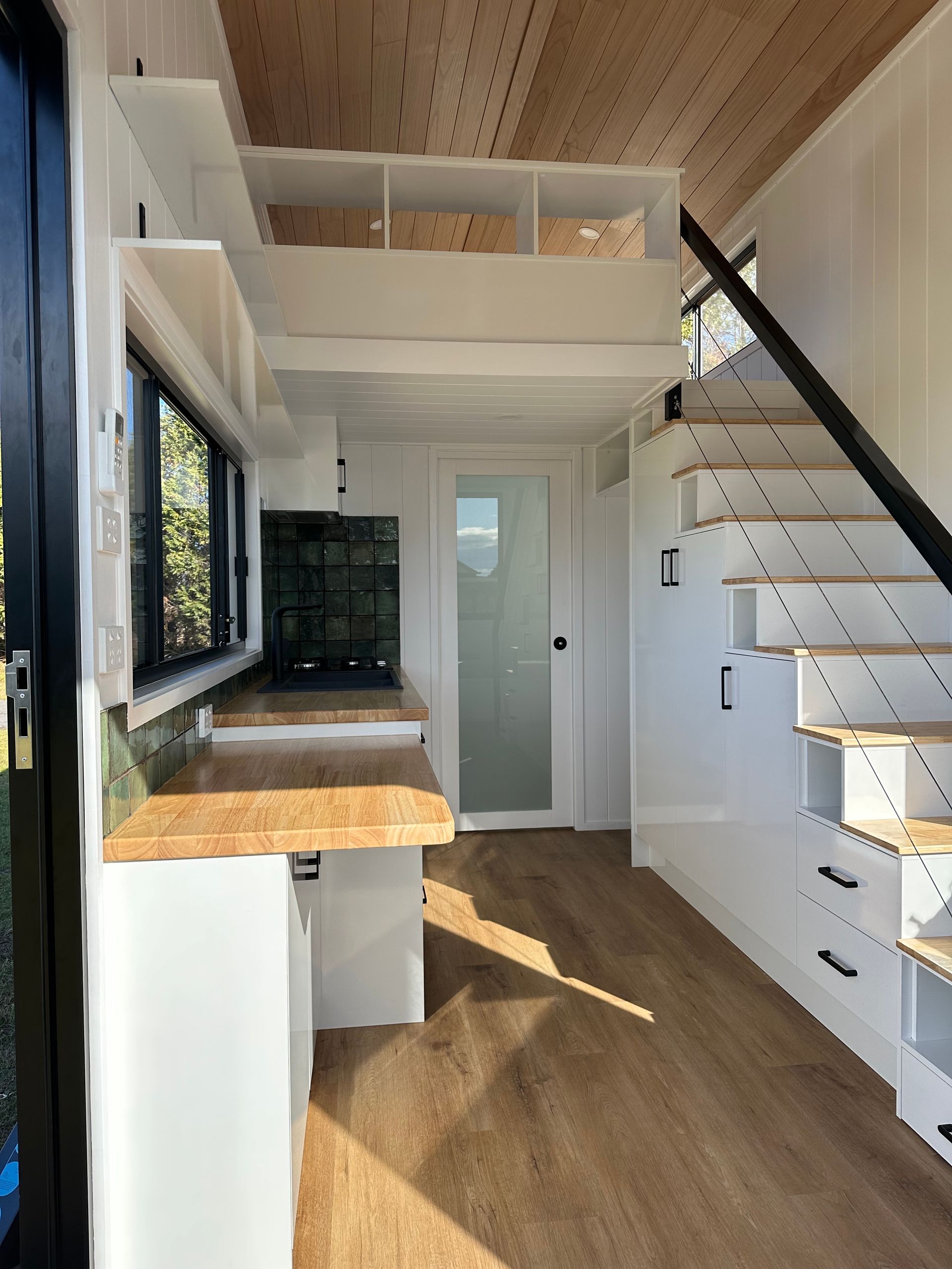 Tiny home interior: kitchen with wood counters, stairs to loft, white walls, and wood ceiling.