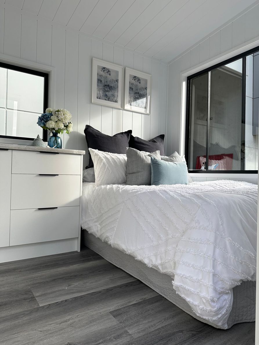 Cozy interior of a tiny home with a couch, ladder, artwork, and a view into a bedroom.