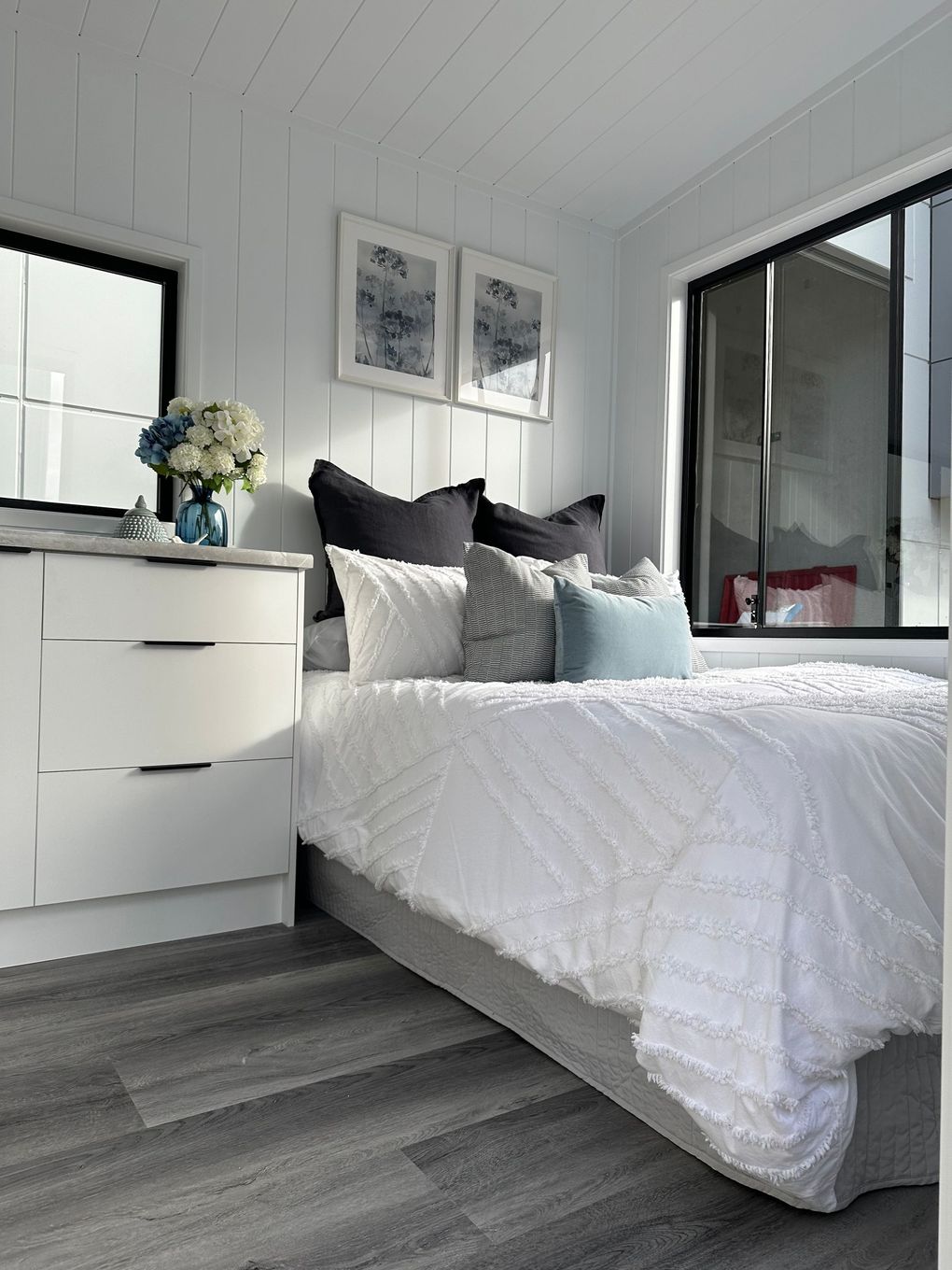 Cozy interior of a tiny home with a couch, ladder, artwork, and a view into a bedroom.