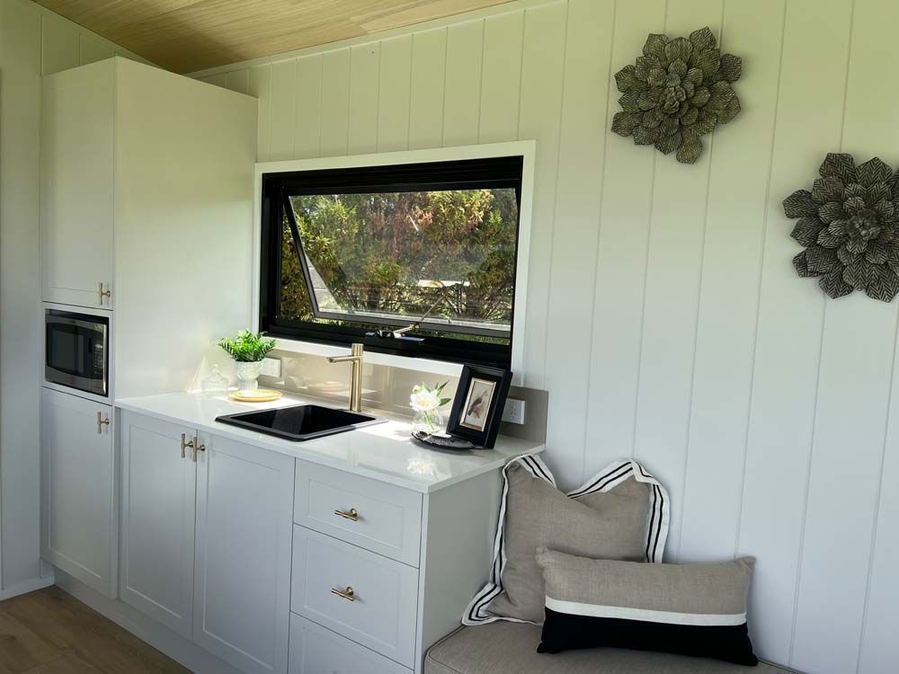 White kitchen with black window, sink, and microwave. Two decorative moss balls on the wall.