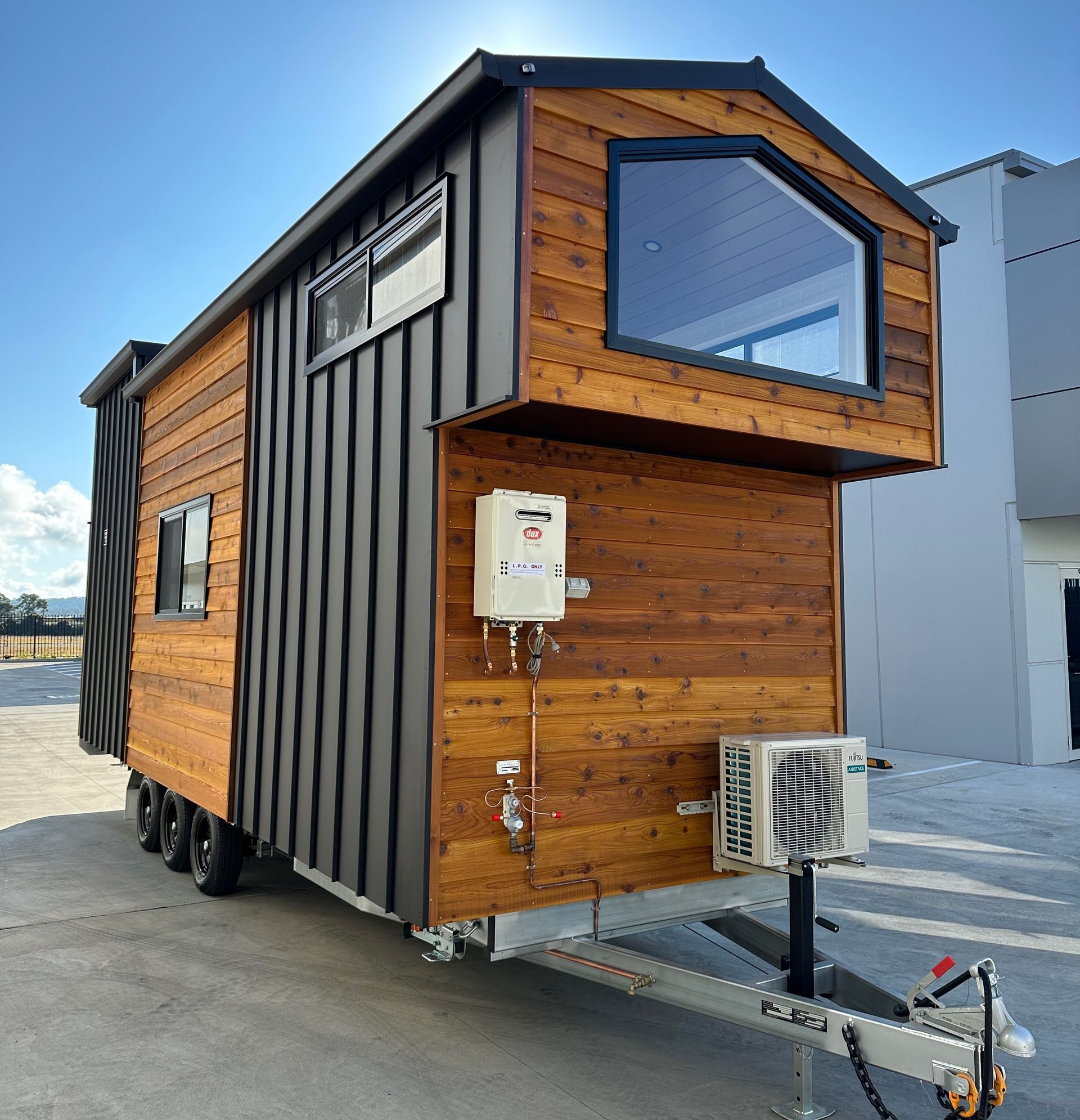 Tiny house on a trailer with wood siding and black metal accents, blue sky.