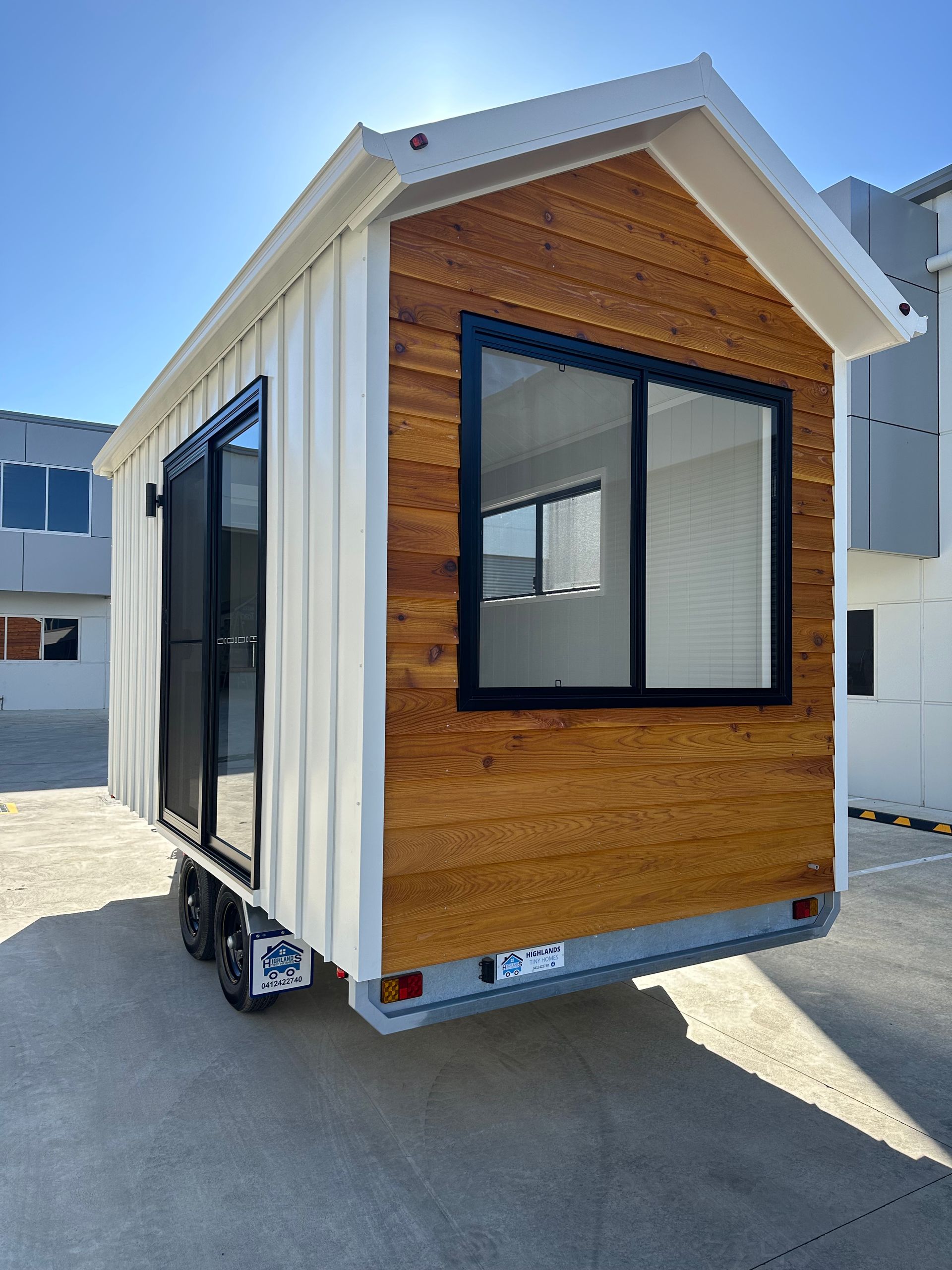 Tiny house on wheels with wood and white siding, black windows and door, parked outside.