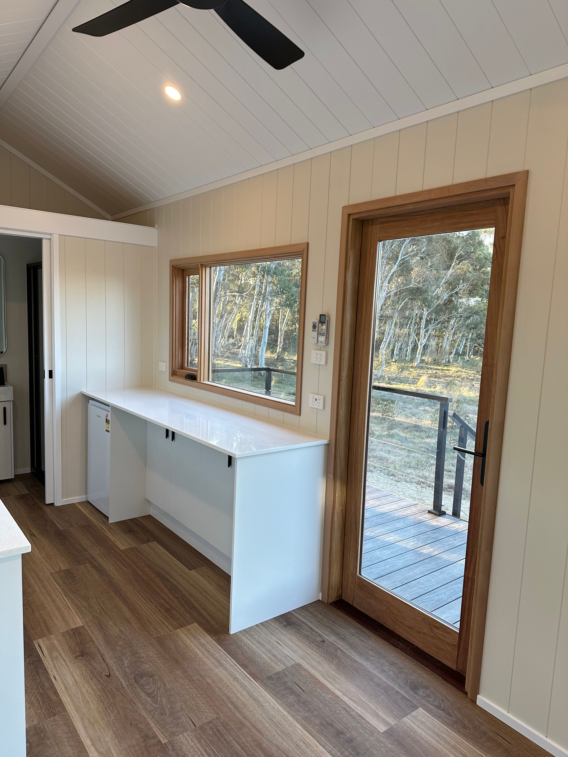 Interior of tiny home with white cabinets, window, and door to a deck.