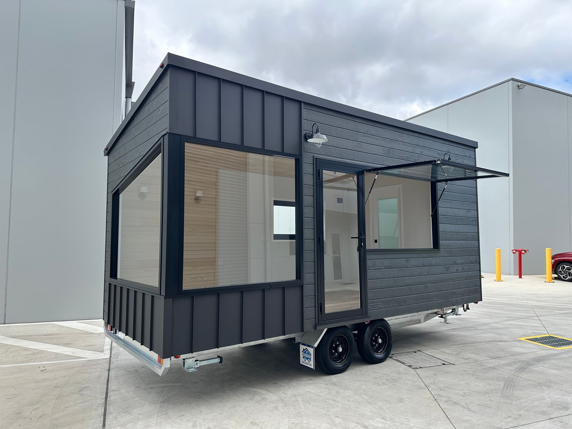 Tiny house on wheels with wood and dark gray metal siding, parked on grass.