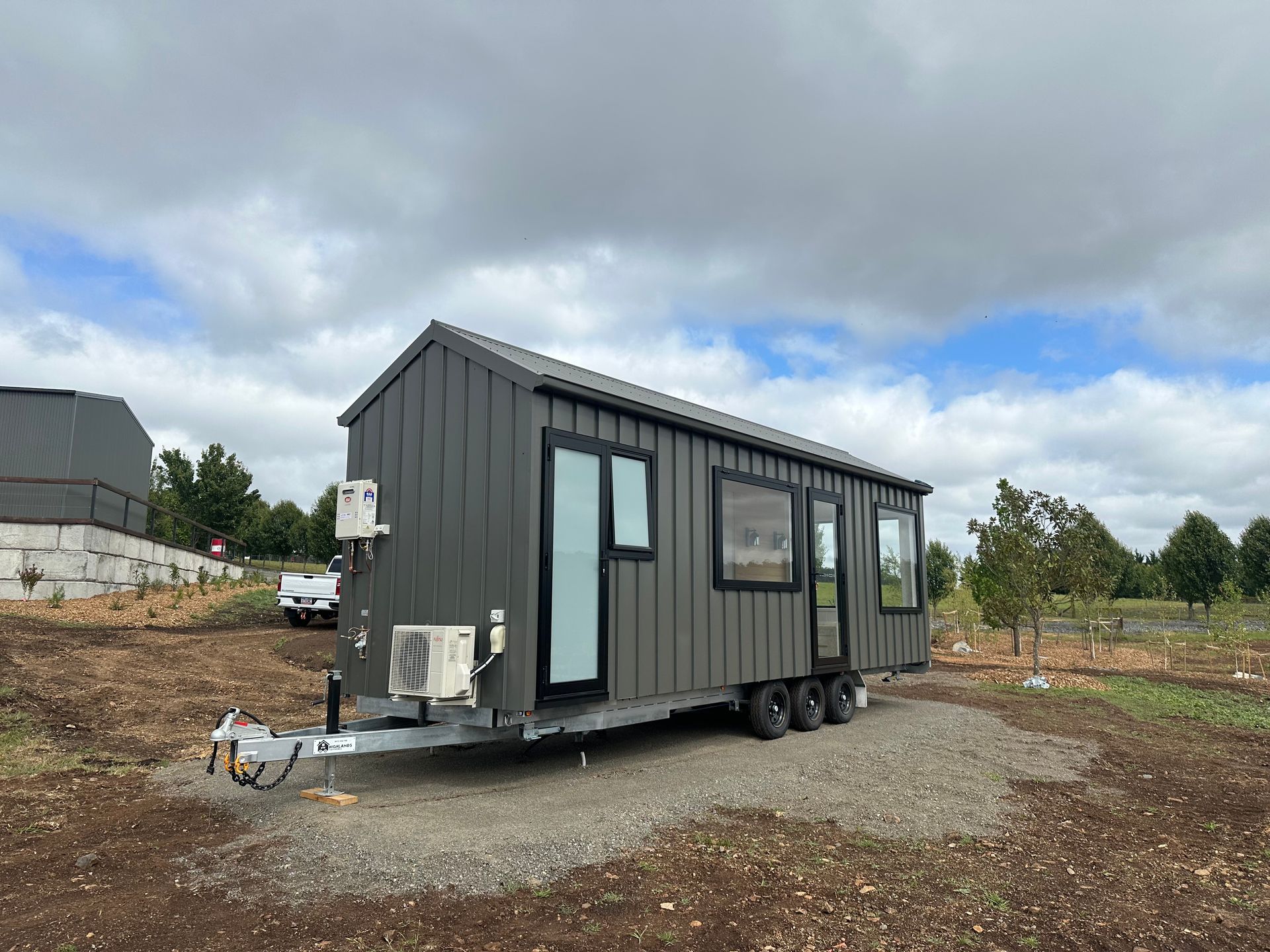 Dark gray tiny house on a trailer, with a gray sky background.