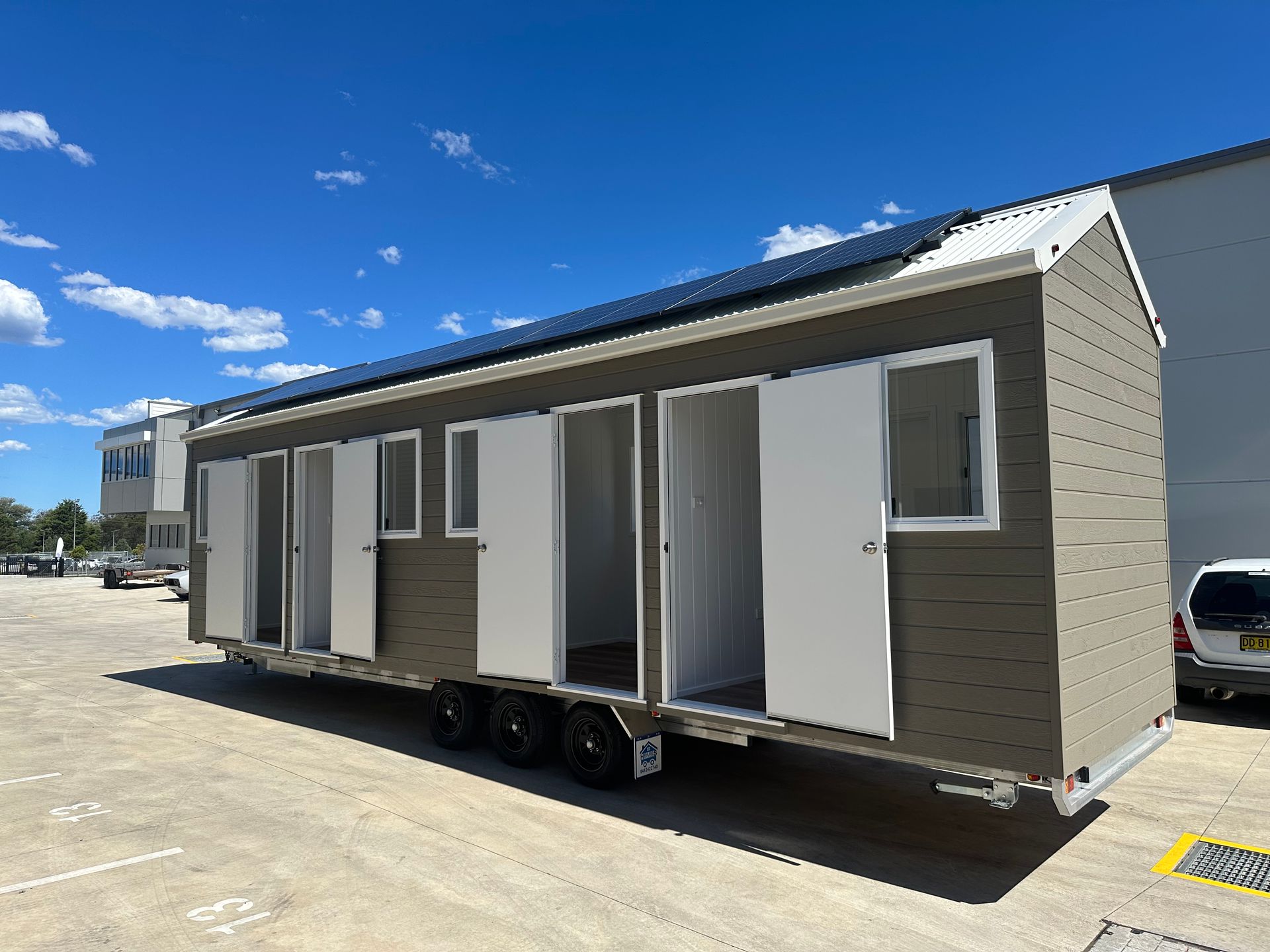 A mobile, brown structure with white doors and windows, set on a trailer. Solar panels on roof.