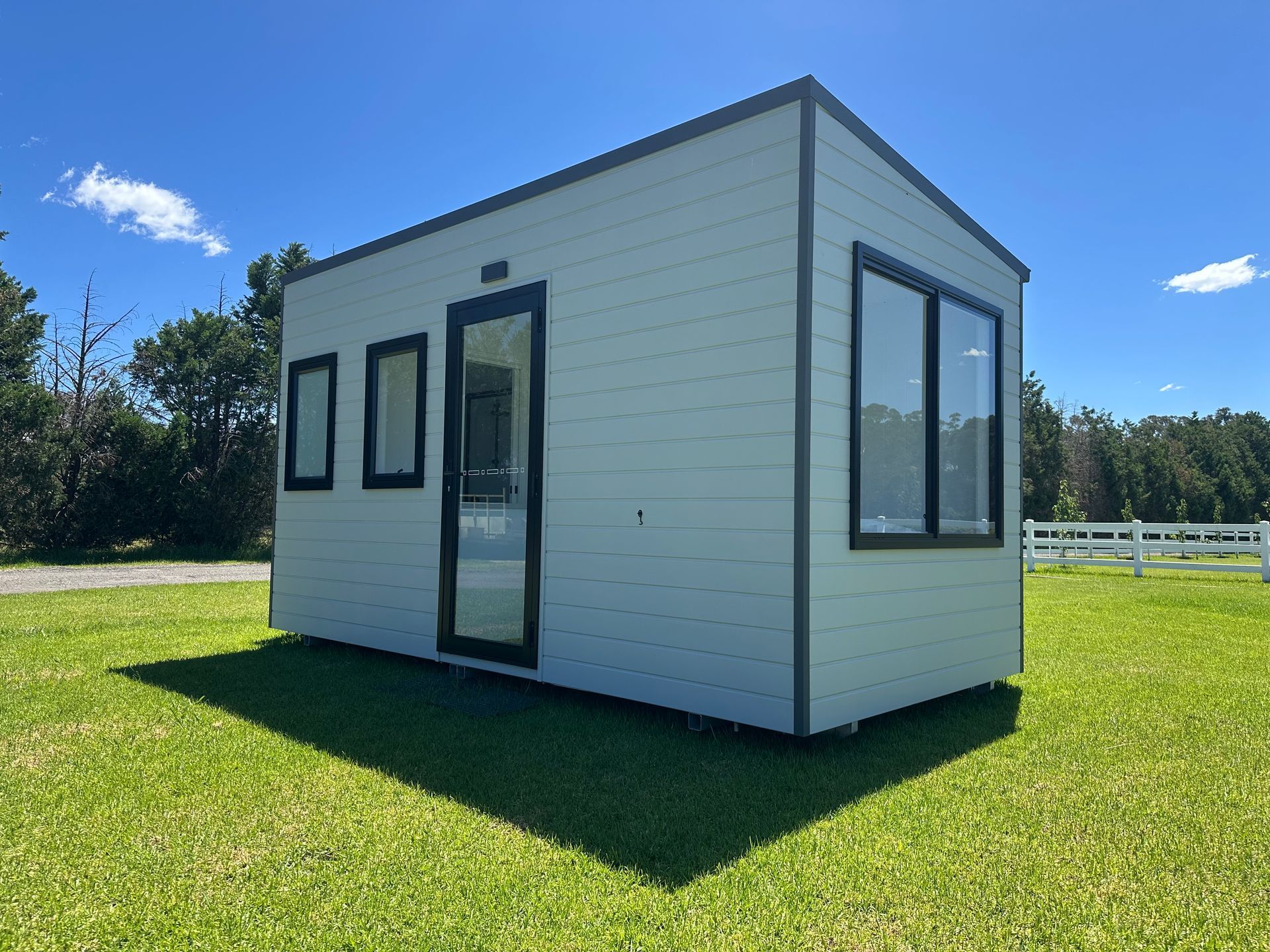 White modular building with black trim and windows on a grassy field under a blue sky.