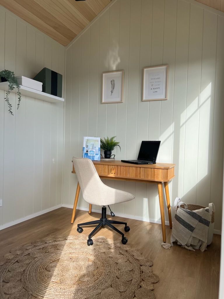 Cozy home office with desk, chair, and laptop. Green walls, wooden desk, and natural light streaming in.