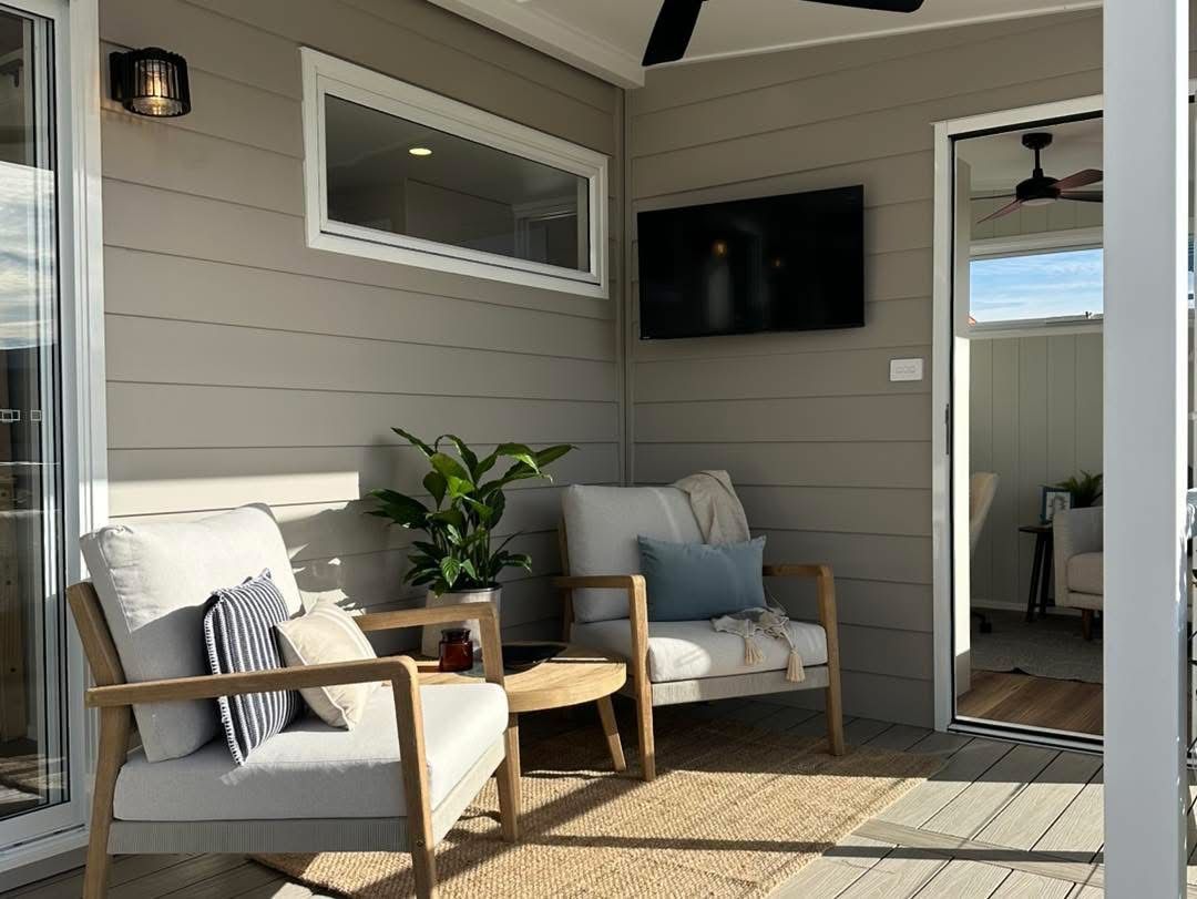 Outdoor seating area with two armchairs, a small table, and a TV mounted on the wall.