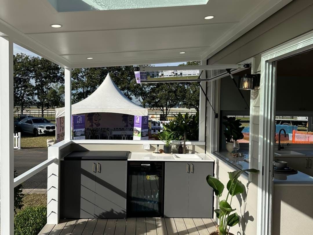 Outdoor kitchen with grey cabinets, sink, and a refrigerator. White gazebo in the background.