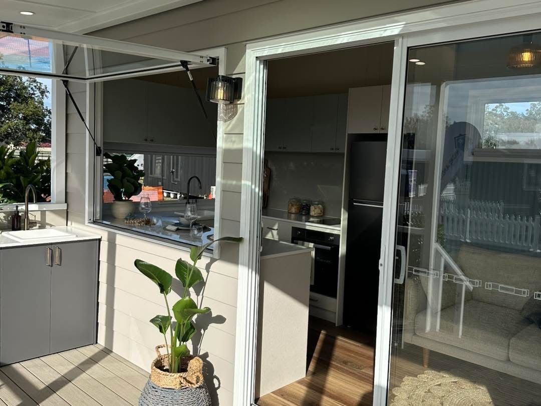 Outdoor kitchen with grey cabinets, stainless steel appliances, and potted plants.