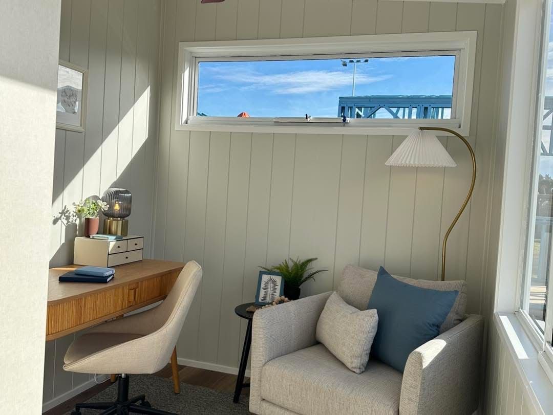 Cozy home office nook with desk, armchair, and window overlooking a sunny sky.
