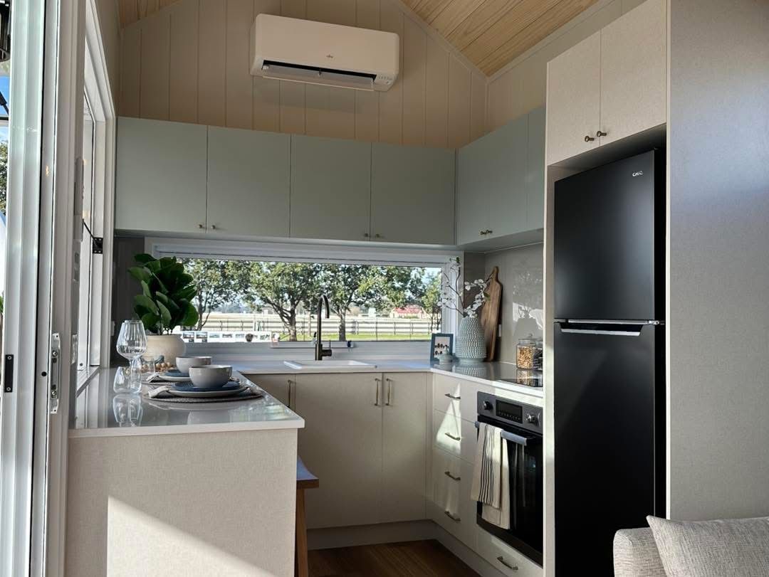 Small kitchen with light blue cabinets, black refrigerator, and window overlooking a field.