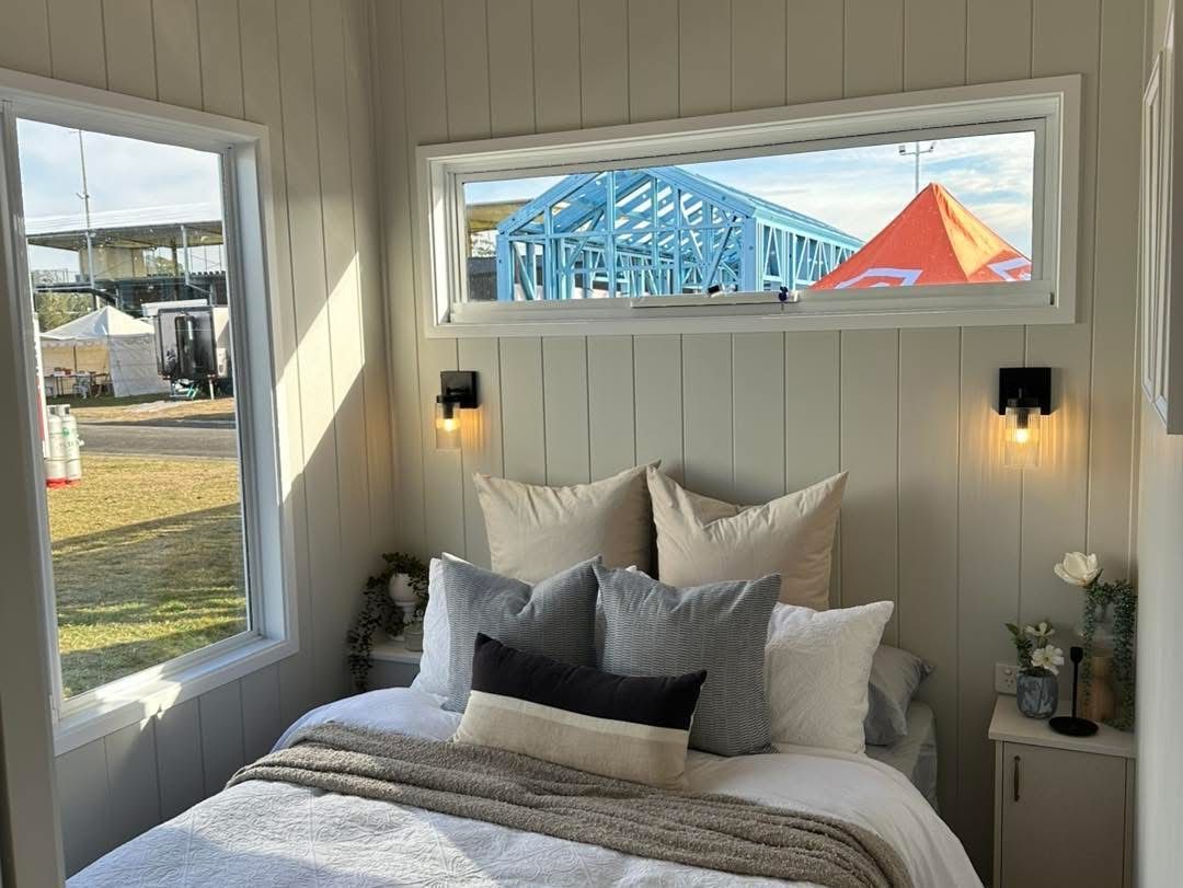 Bedroom with bed and pillows, two windows, and view of a building under construction outdoors.