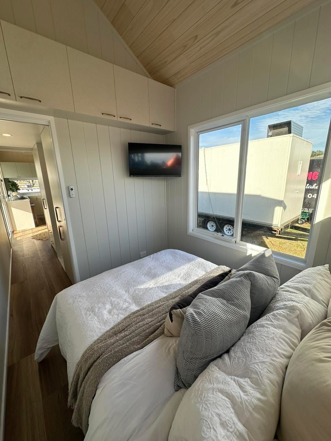 Cozy bedroom with a bed, pillows, TV, and window overlooking a trailer.