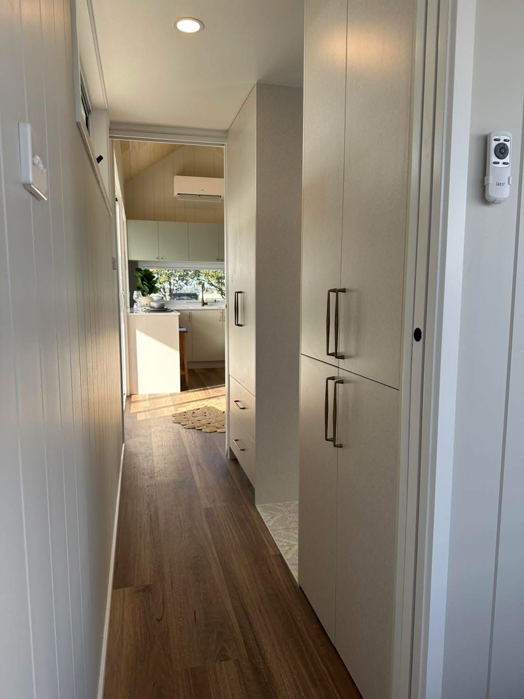 Narrow hallway with white cabinetry and wood flooring leading to a kitchen.